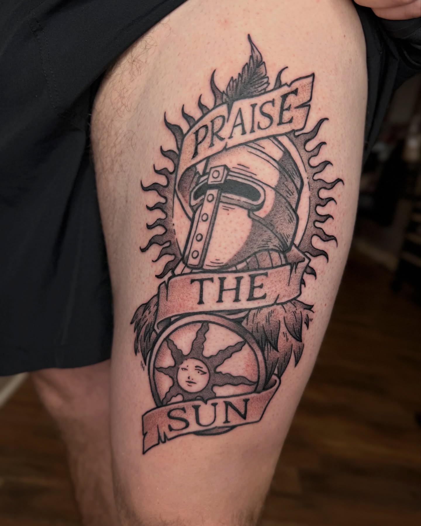 Sun and helmet black and grey tattoo on the thigh by Jezza Munson