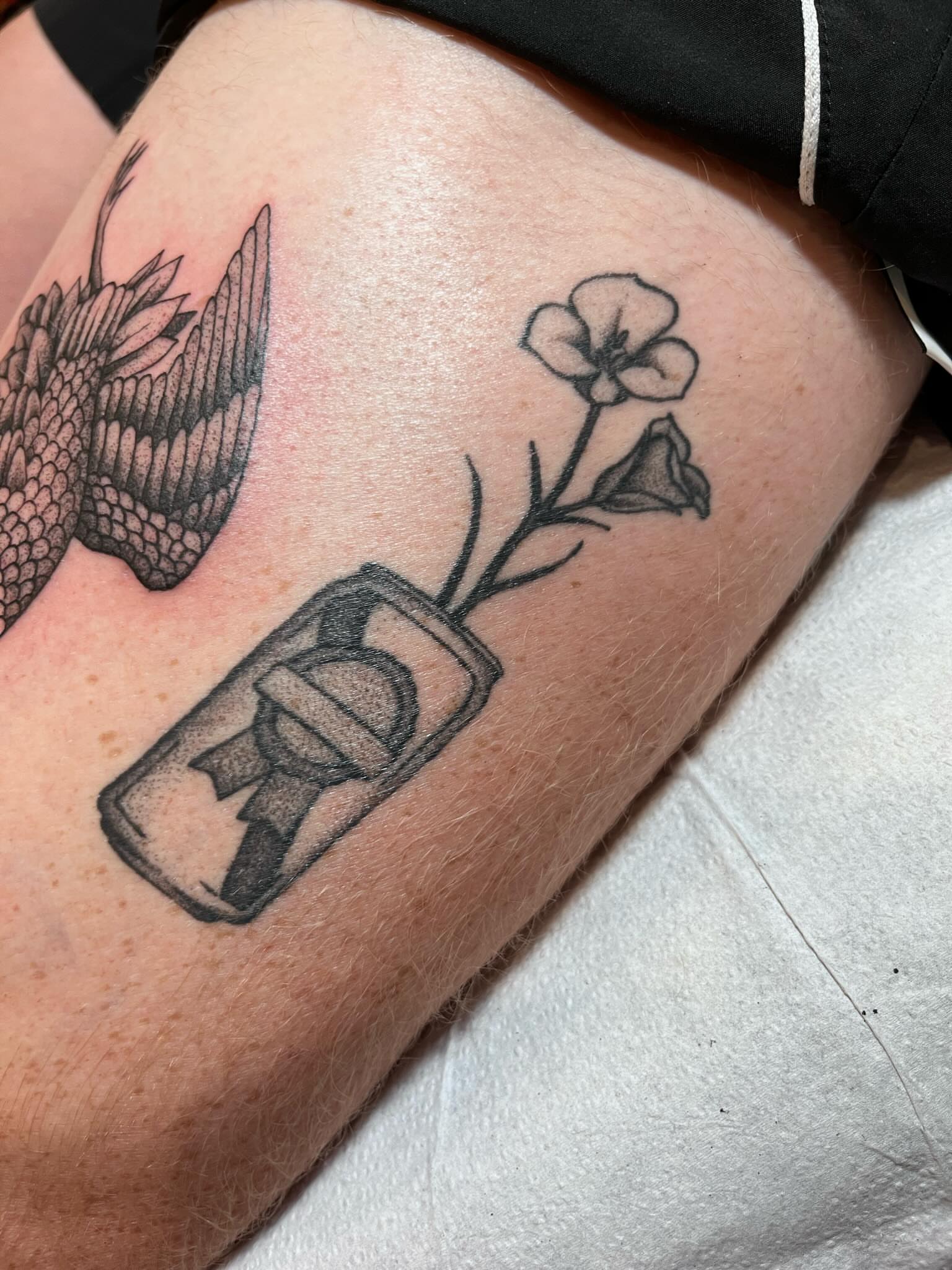 Flower and bottle black and grey tattoo on the thigh by Jackson Kirchhoff