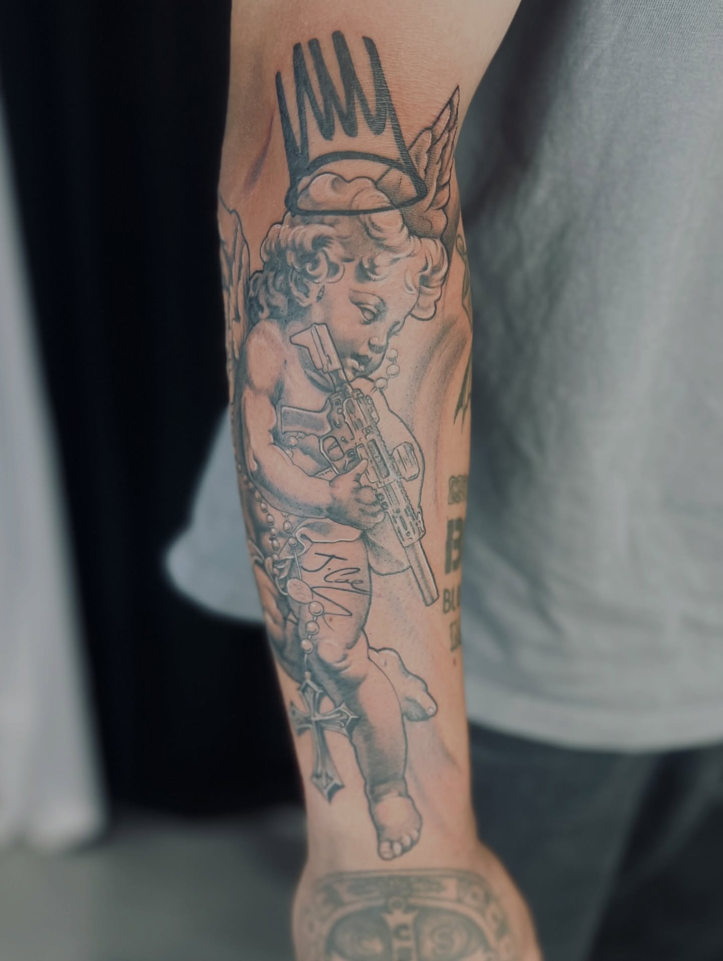Cherub with rifle neo-traditional tattoo on the forearm by Apologies tattoo studios.