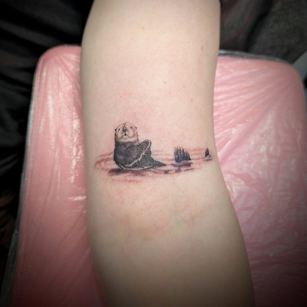 Sea otter floating in water realism tattoo on the forearm by Rhiannon