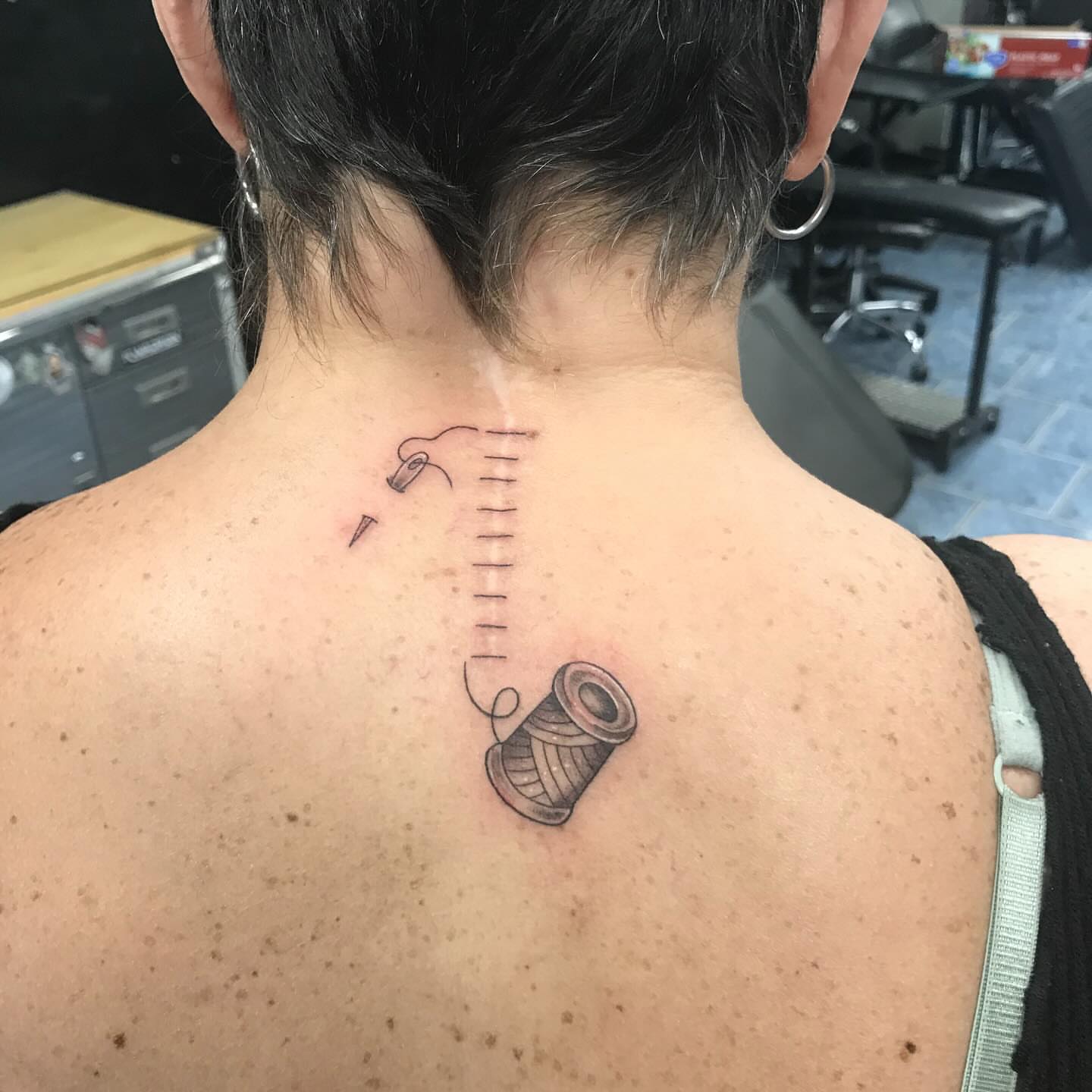 Thread spool and needle black and grey tattoo on the back by @artinjections667