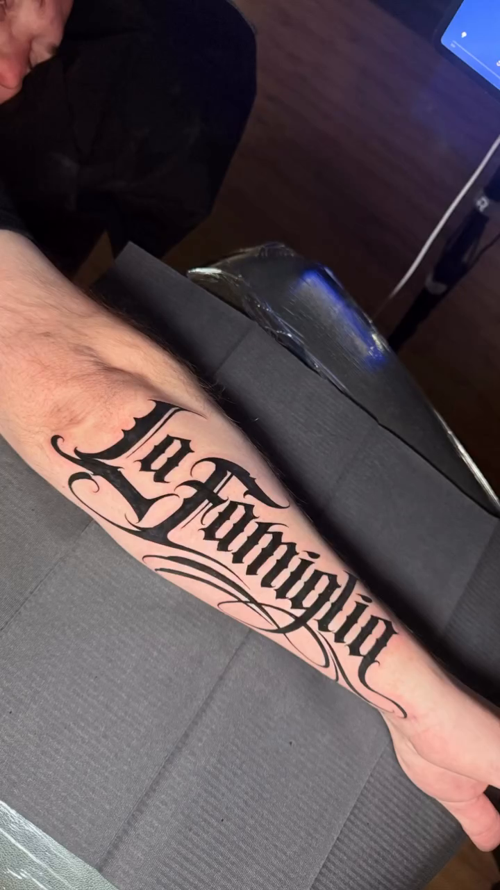 La Famiglia script tattoo lettering tattoo on the forearm by Gilberto Flores Nava