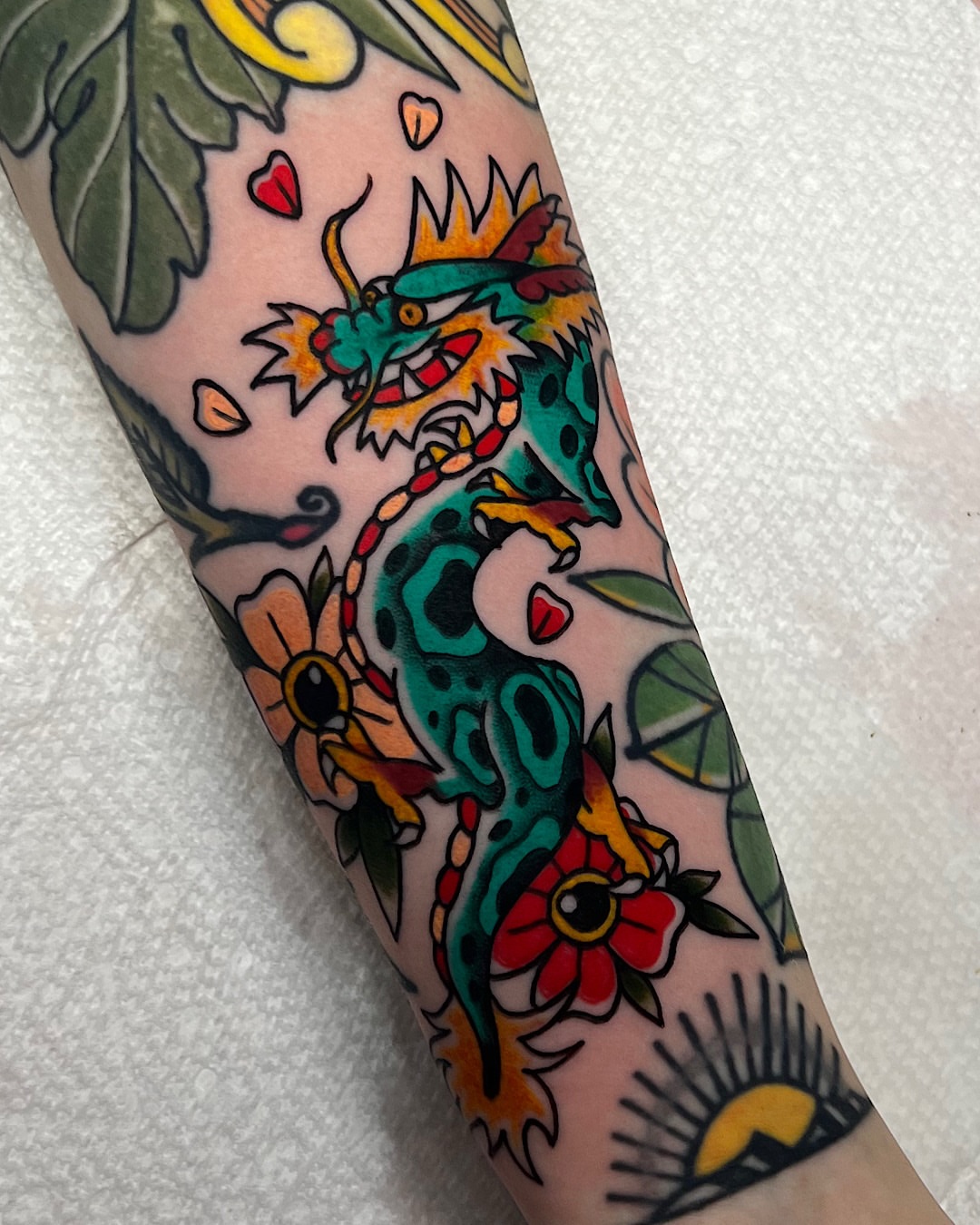 Dragon and flowers American traditional tattoo on the forearm by @shannonkeeleyy