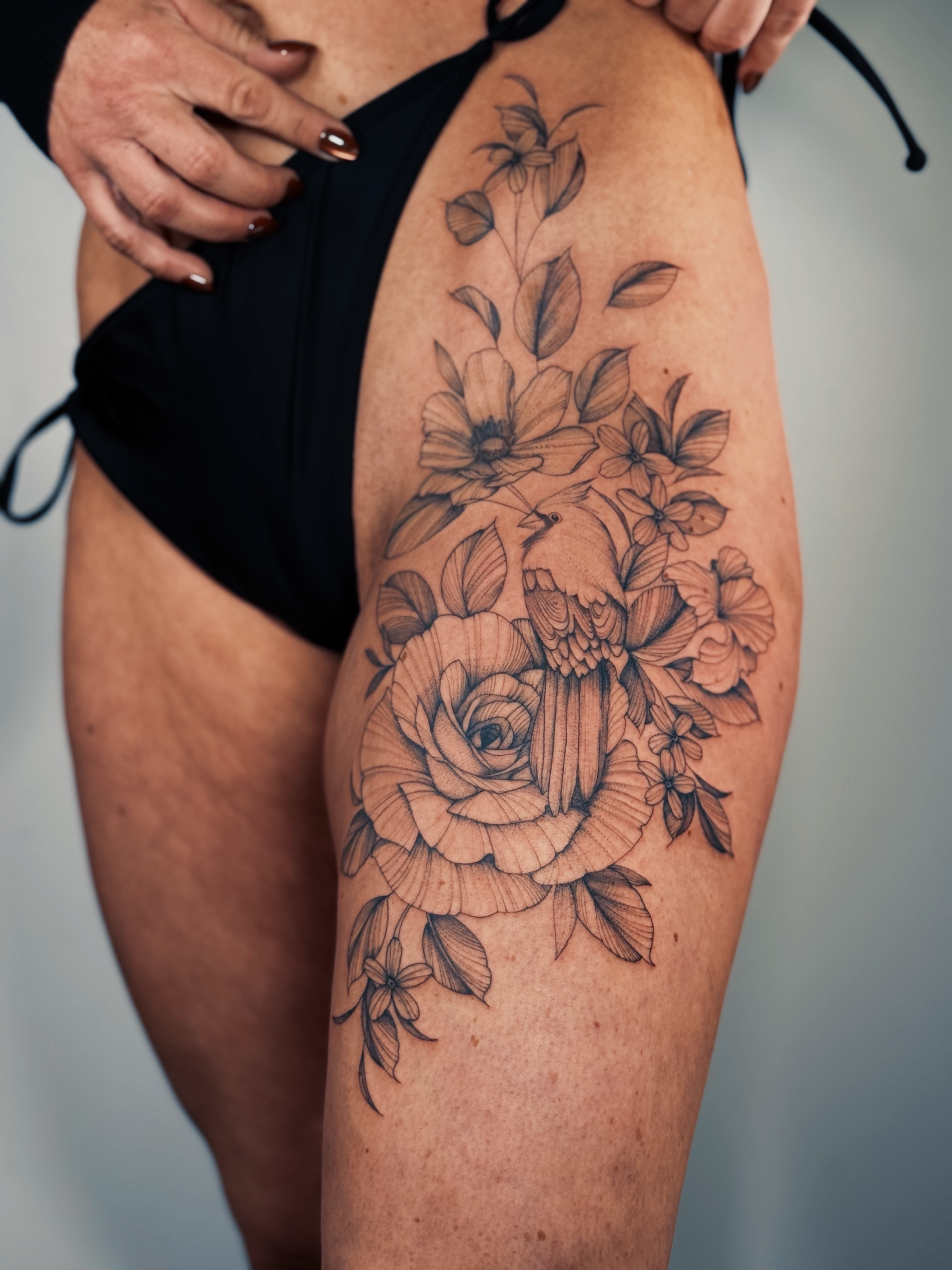 Floral bouquet black and grey tattoo on the thigh by Olha Tytarenko