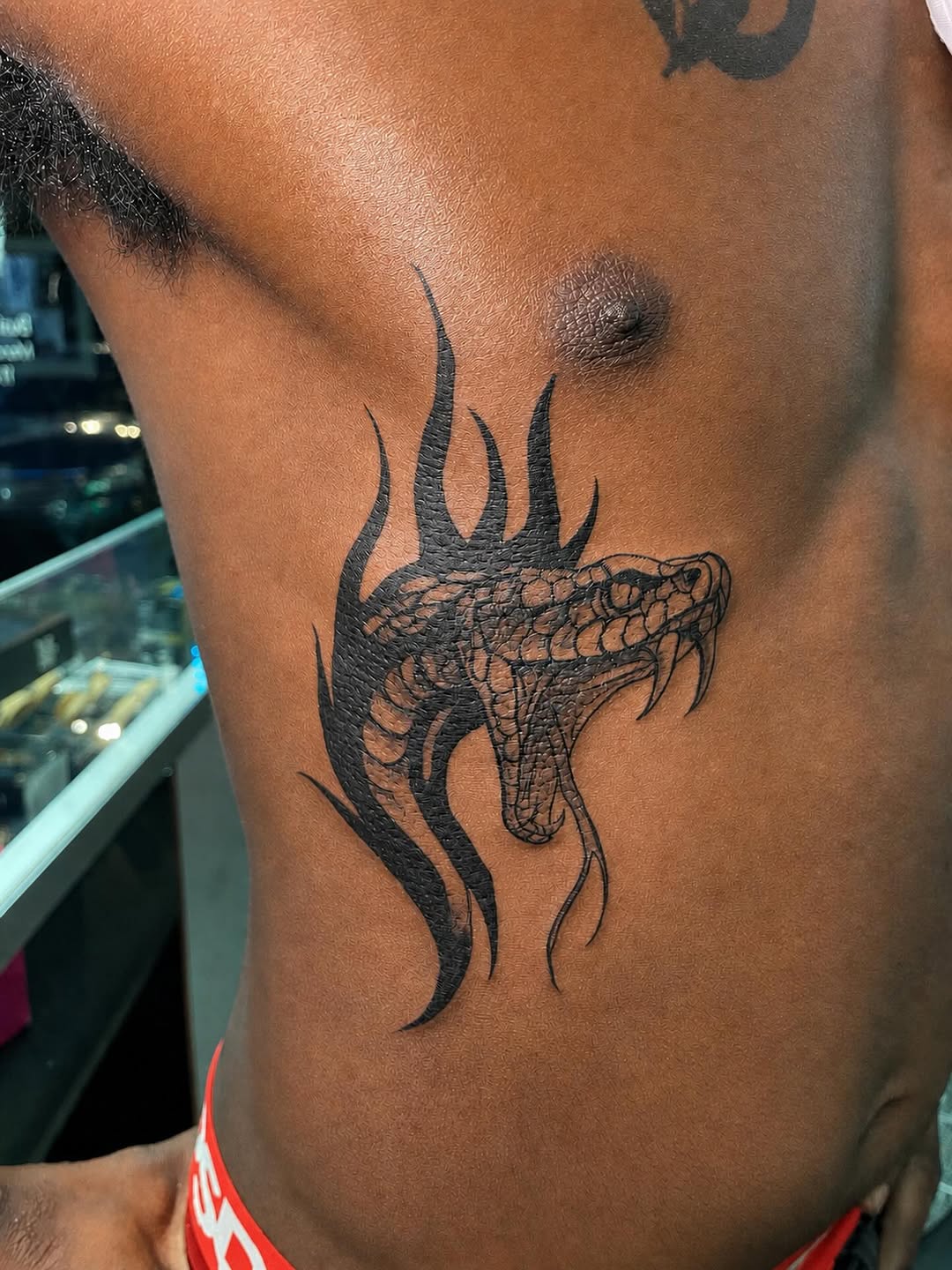 Snake with flames blackwork tattoo on the ribs by 𝚃𝙰𝚃𝚃𝙾𝙾 𝙰𝚁𝚃𝙸𝚂𝚃, Charlotte, North Carolina
