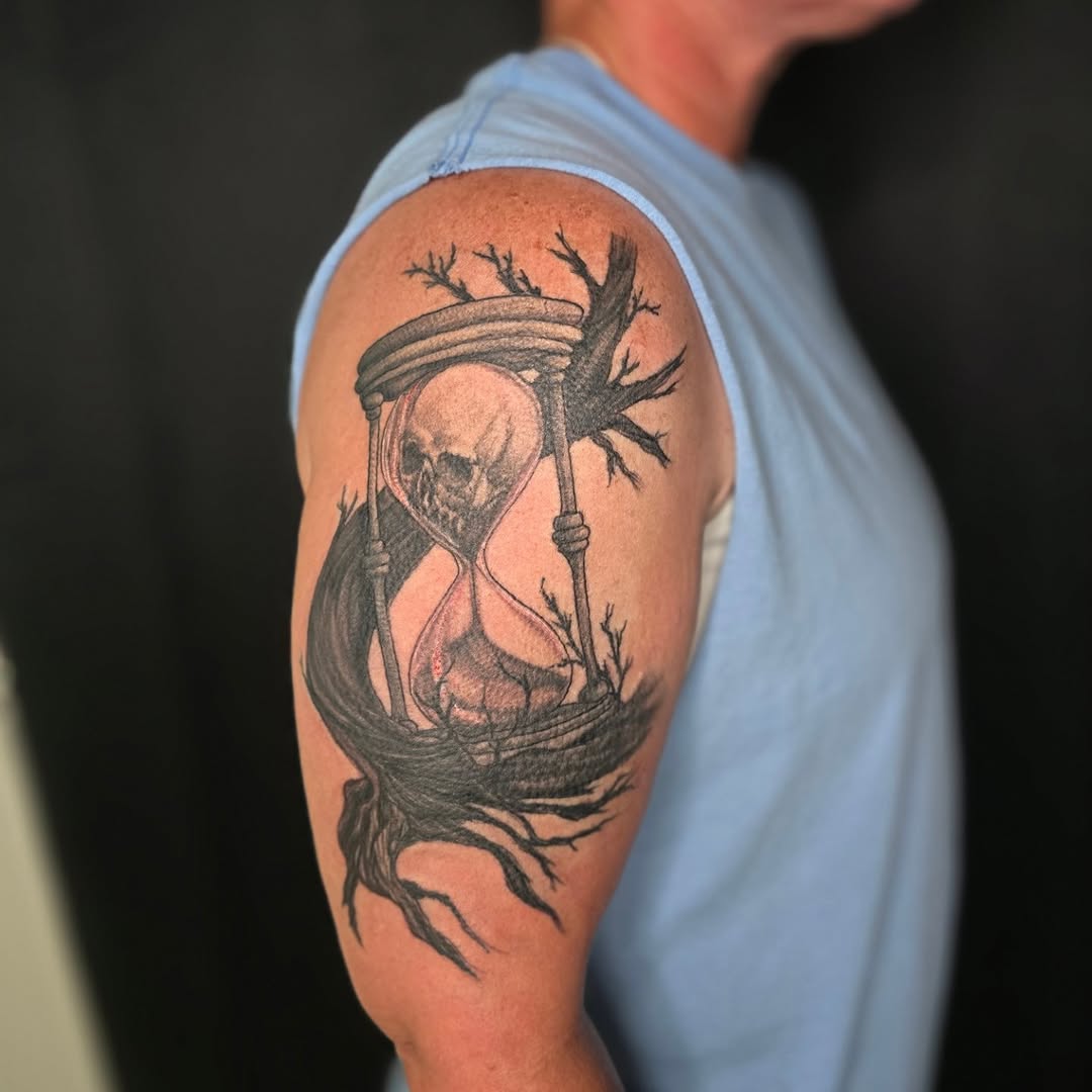 Hourglass with skull and tree branches dark art tattoo on the upper arm by Karen Cain