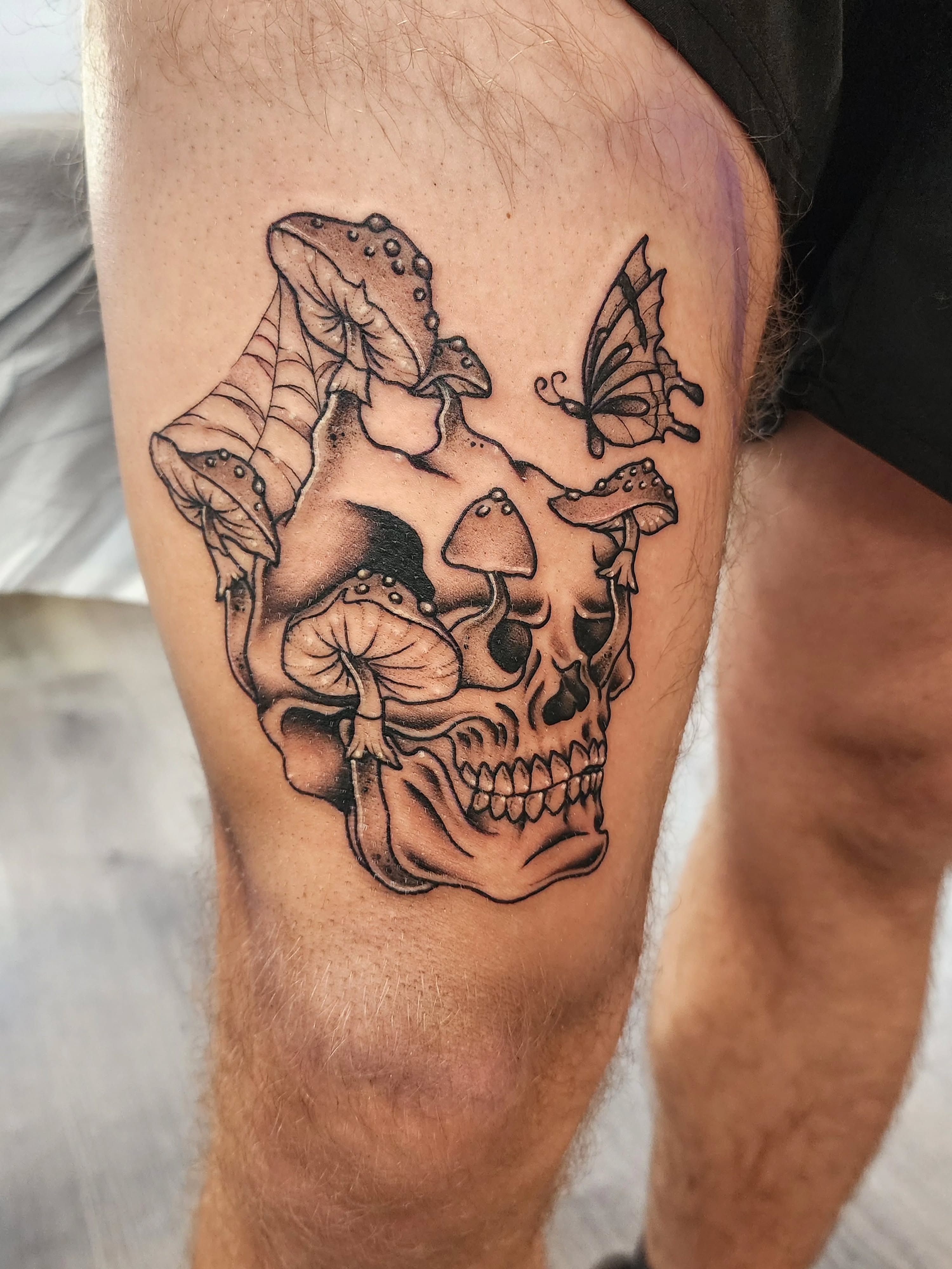 Skull with mushrooms and butterfly realism tattoo on the thigh by mikayla