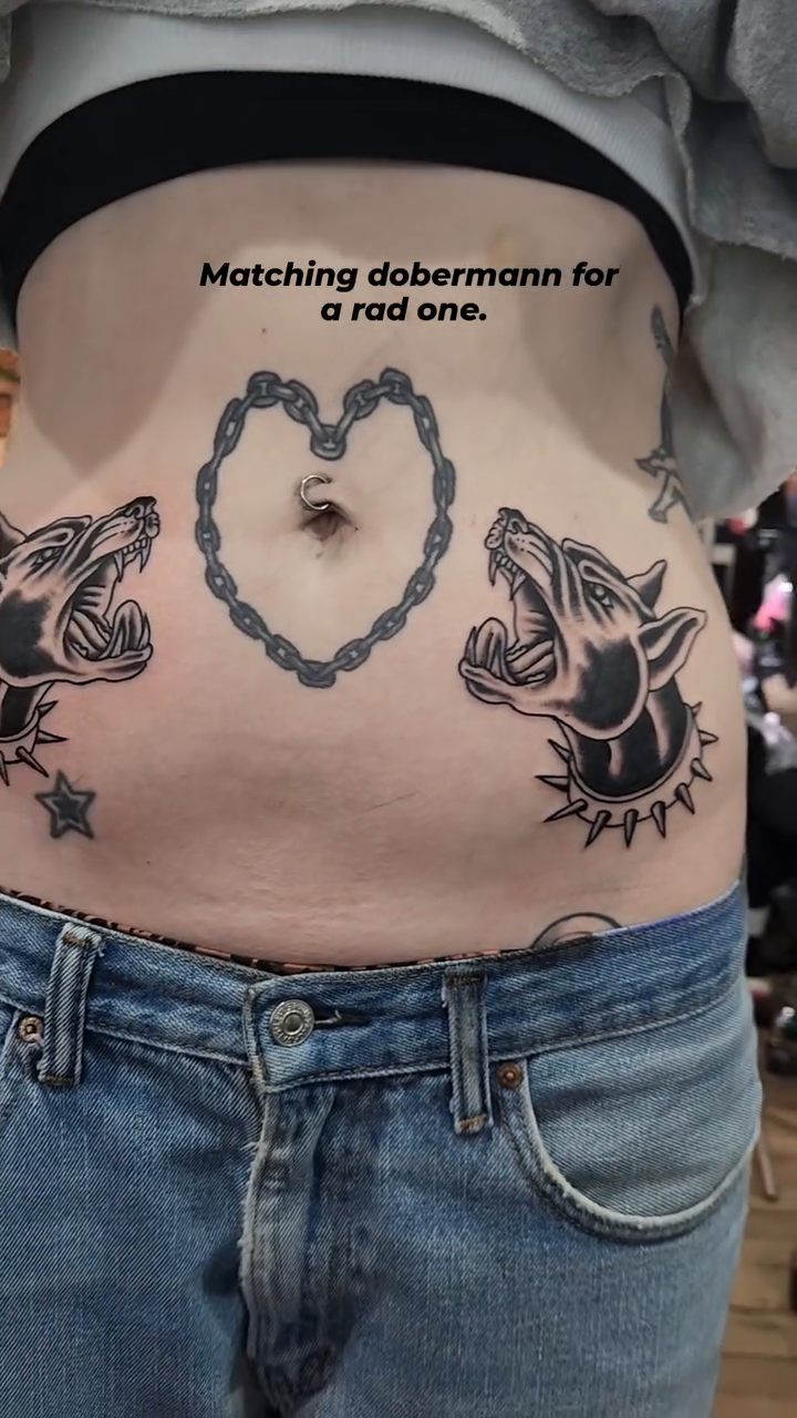 Two dobermans and a heart chain realism tattoo on the torso by Douglas Grady