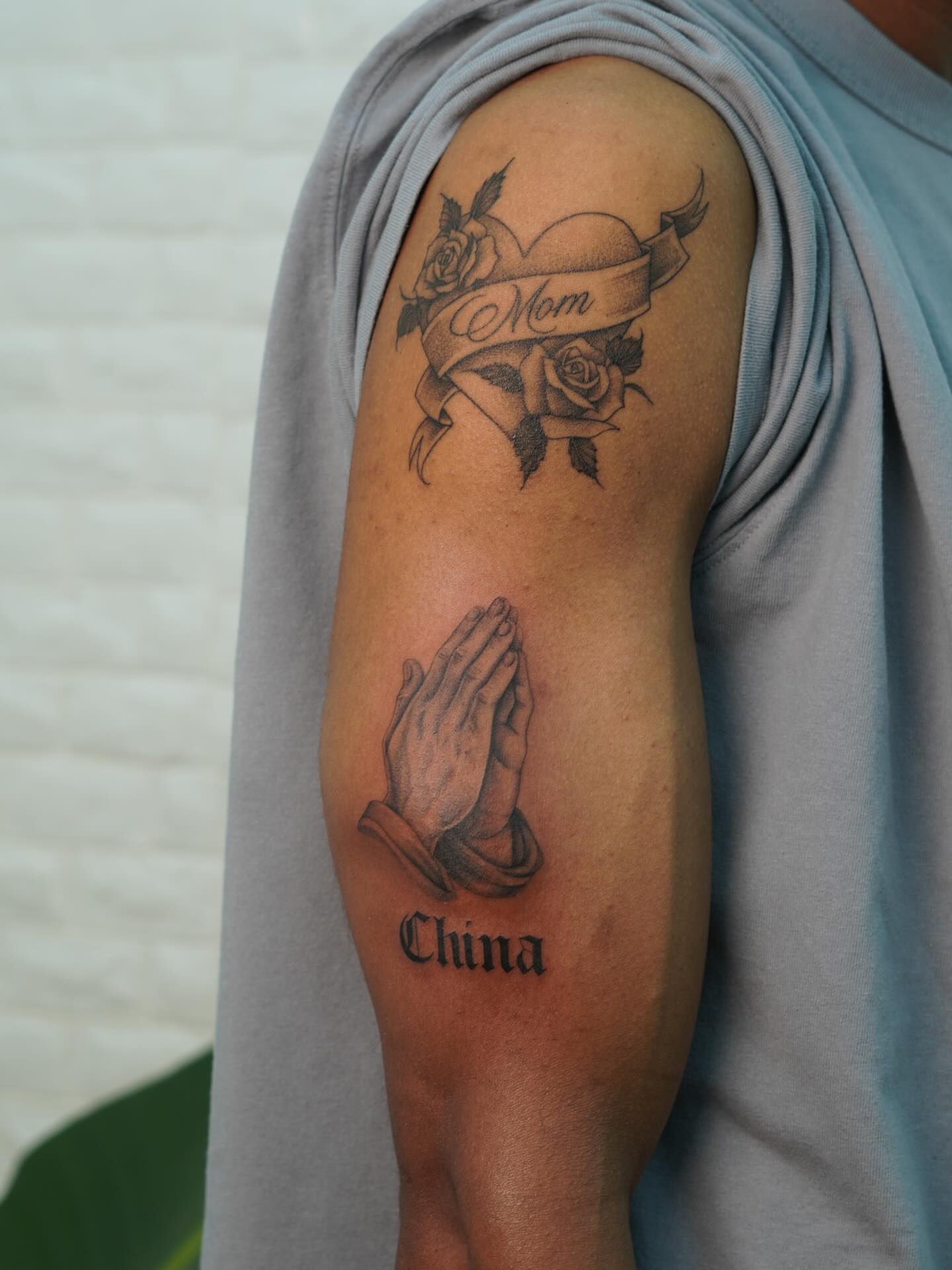 Praying hands and roses black and grey tattoo on the forearm by Danae Andino