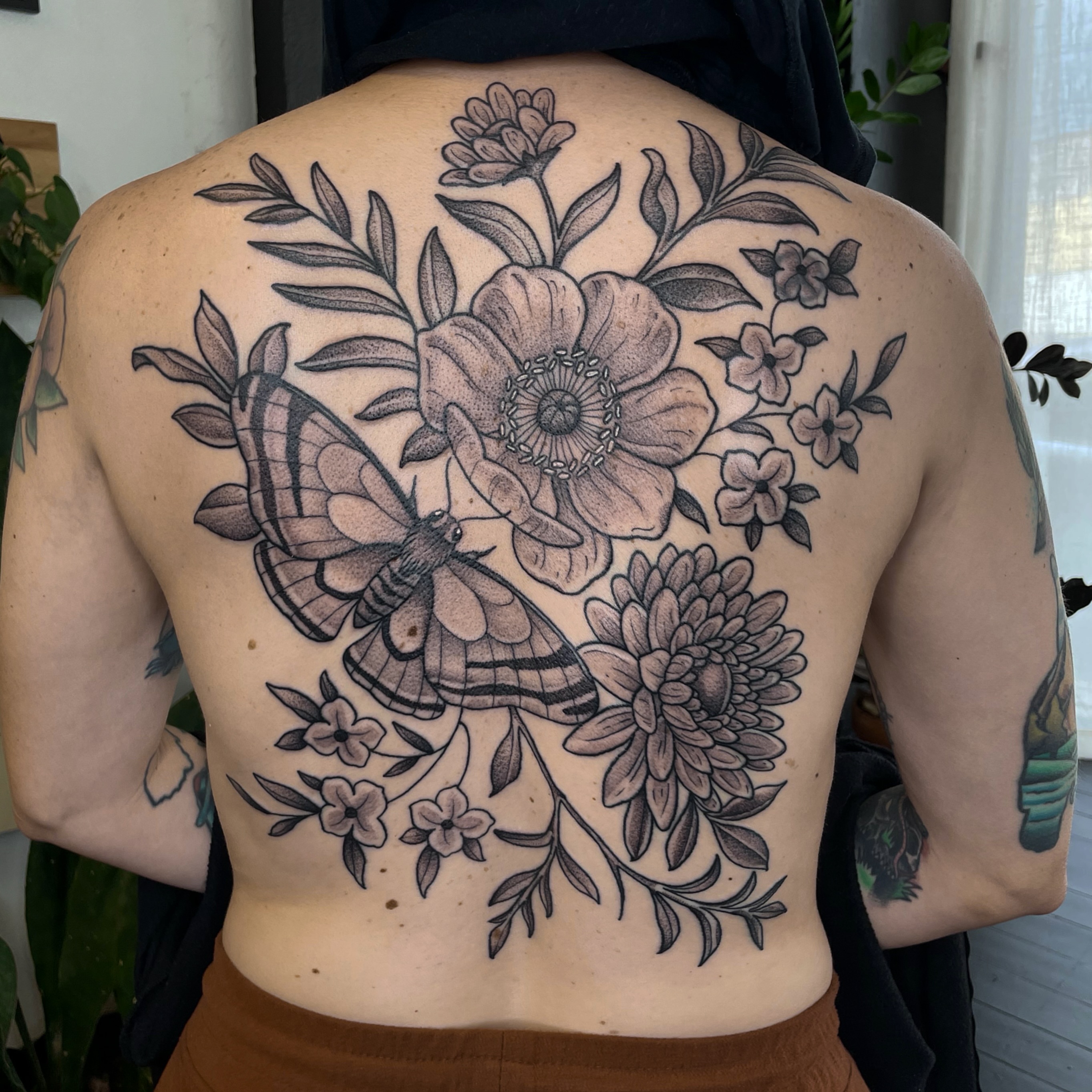 Butterfly and floral bouquet realism tattoo on the back by Emily Lux