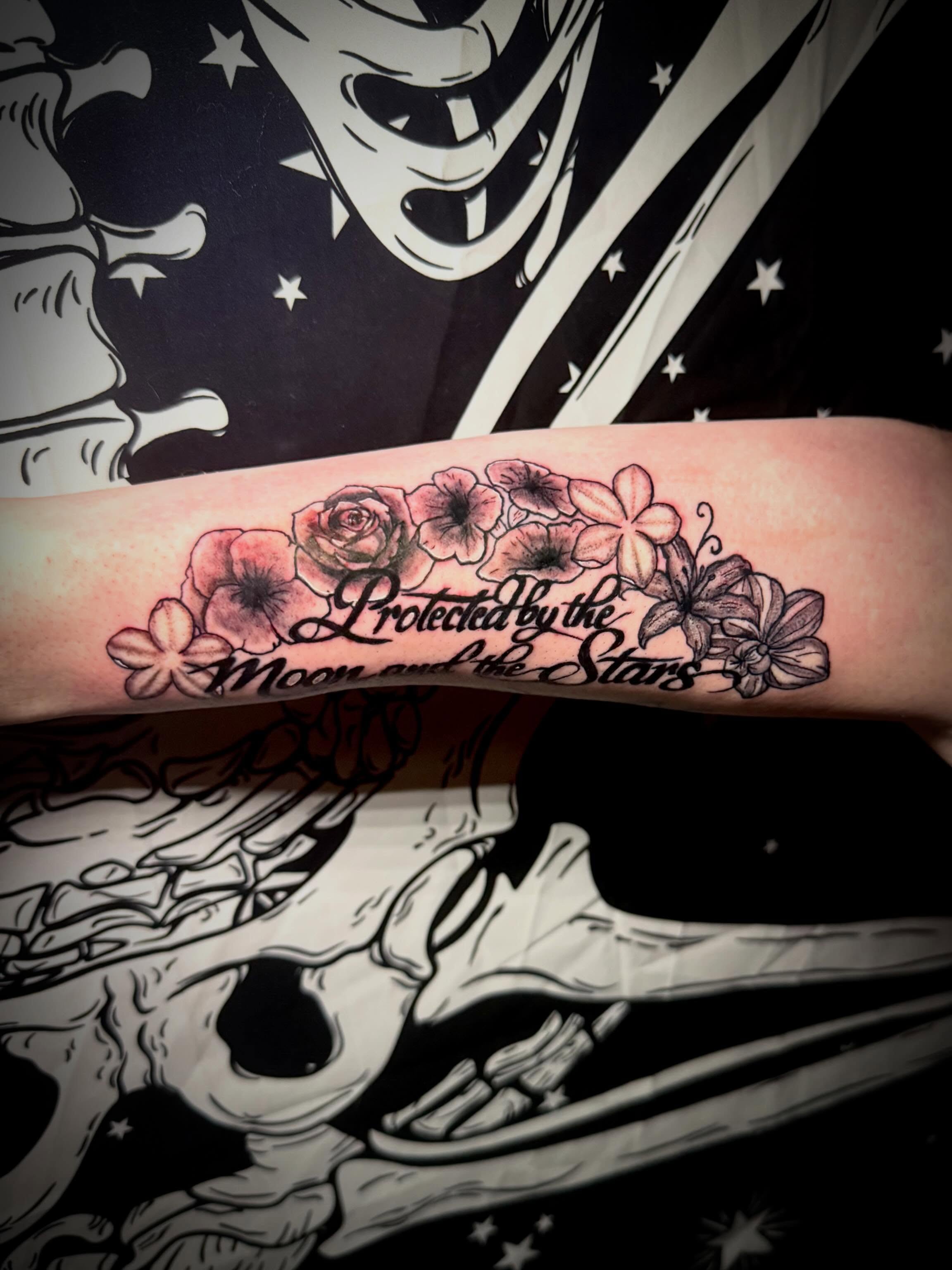 Flowers and text black and grey tattoo on the forearm by Mikey