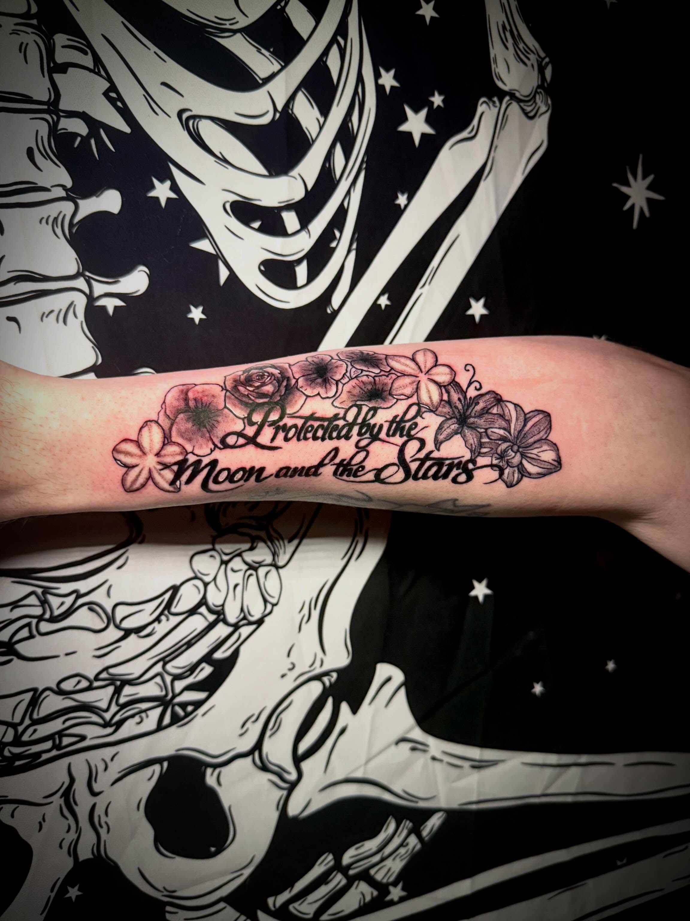 Flowers and script black and grey tattoo on the forearm by Mikey