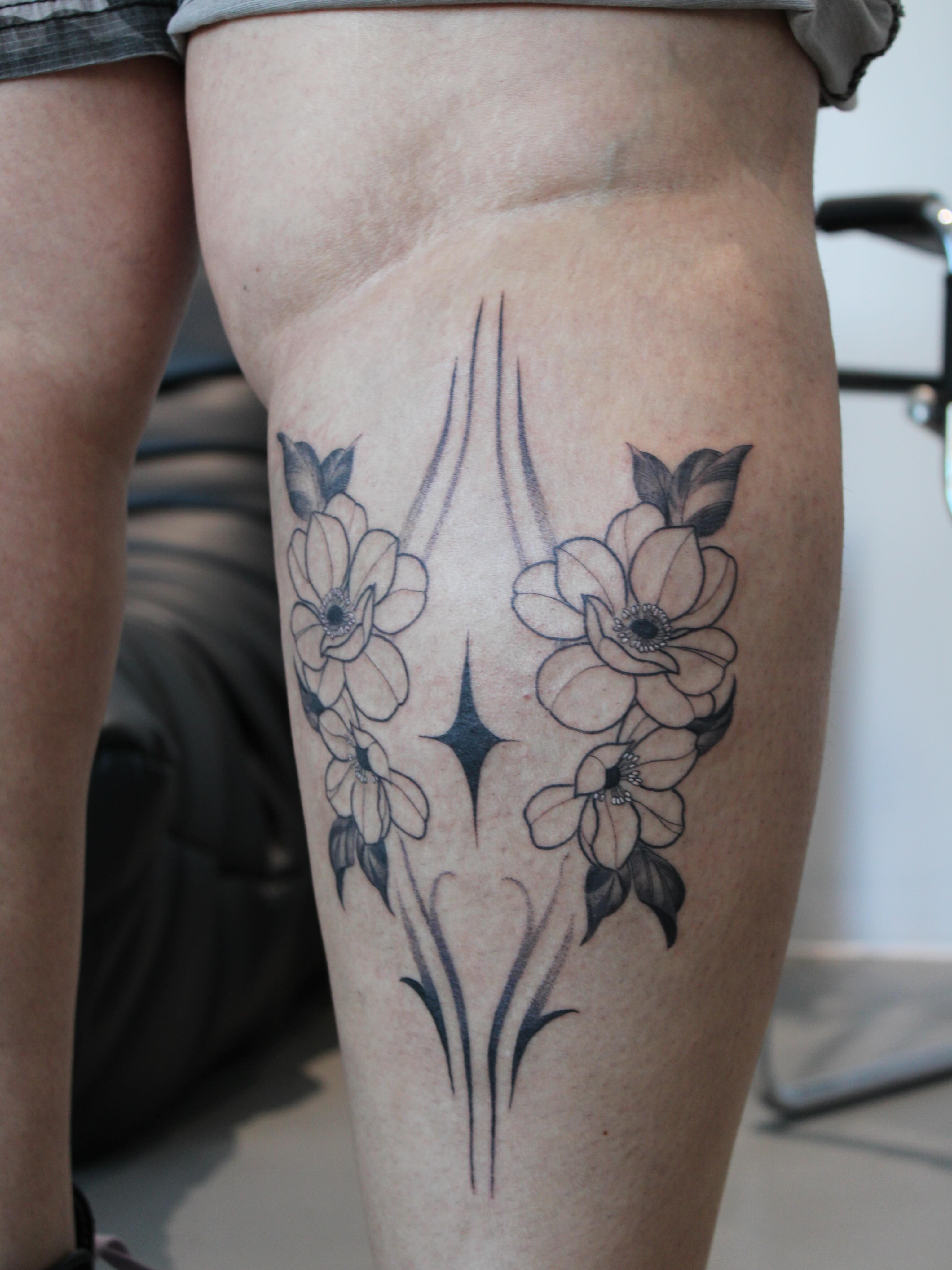 Flowers and starburst black and grey tattoo on the thigh by Julianna