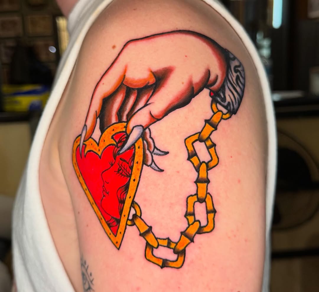Hand holding a heart locket American traditional tattoo on the shoulder by @michaelryan_tattoo