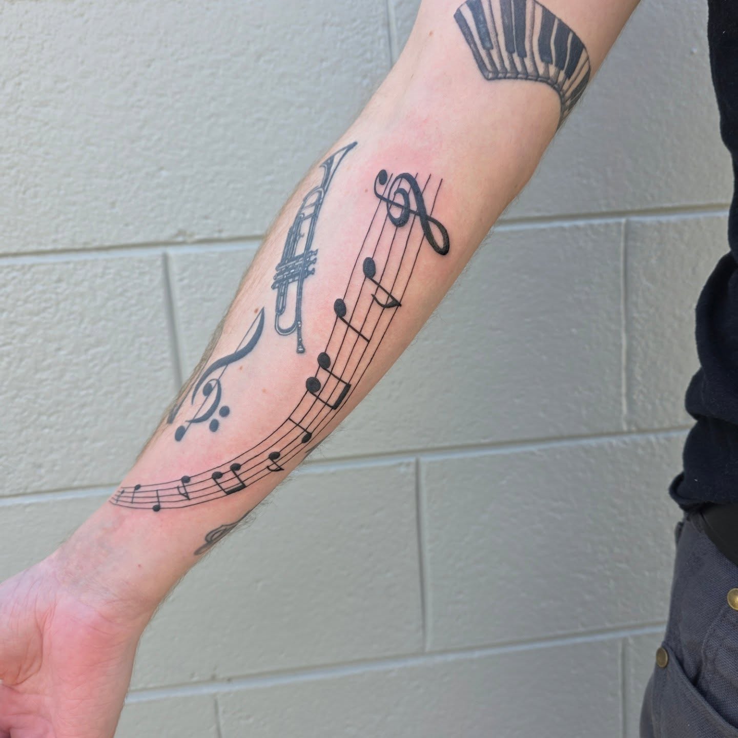 Music notes and trumpet black and grey tattoo on the forearm by Maggie