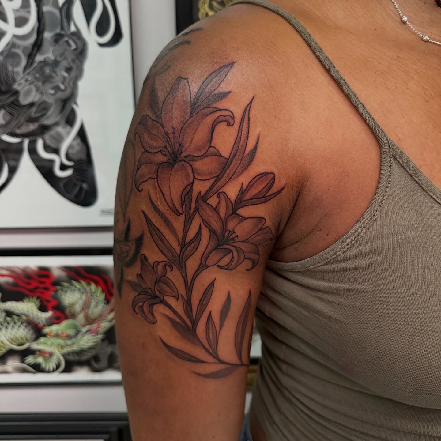 Lilies black and grey tattoo on the upper arm by Mia Layne 🤎