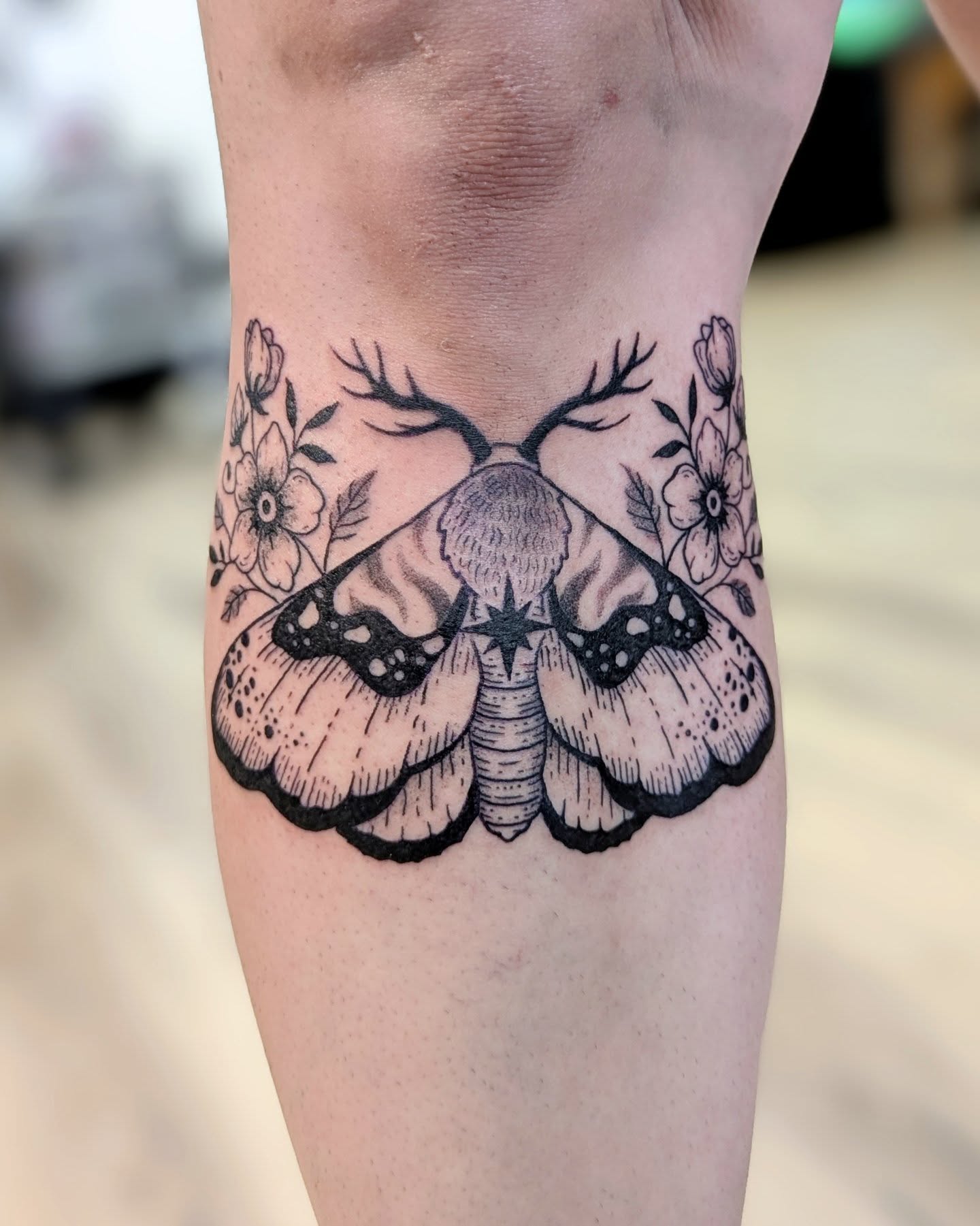 Moth and flowers black and grey tattoo on the forearm by Dani Harkey