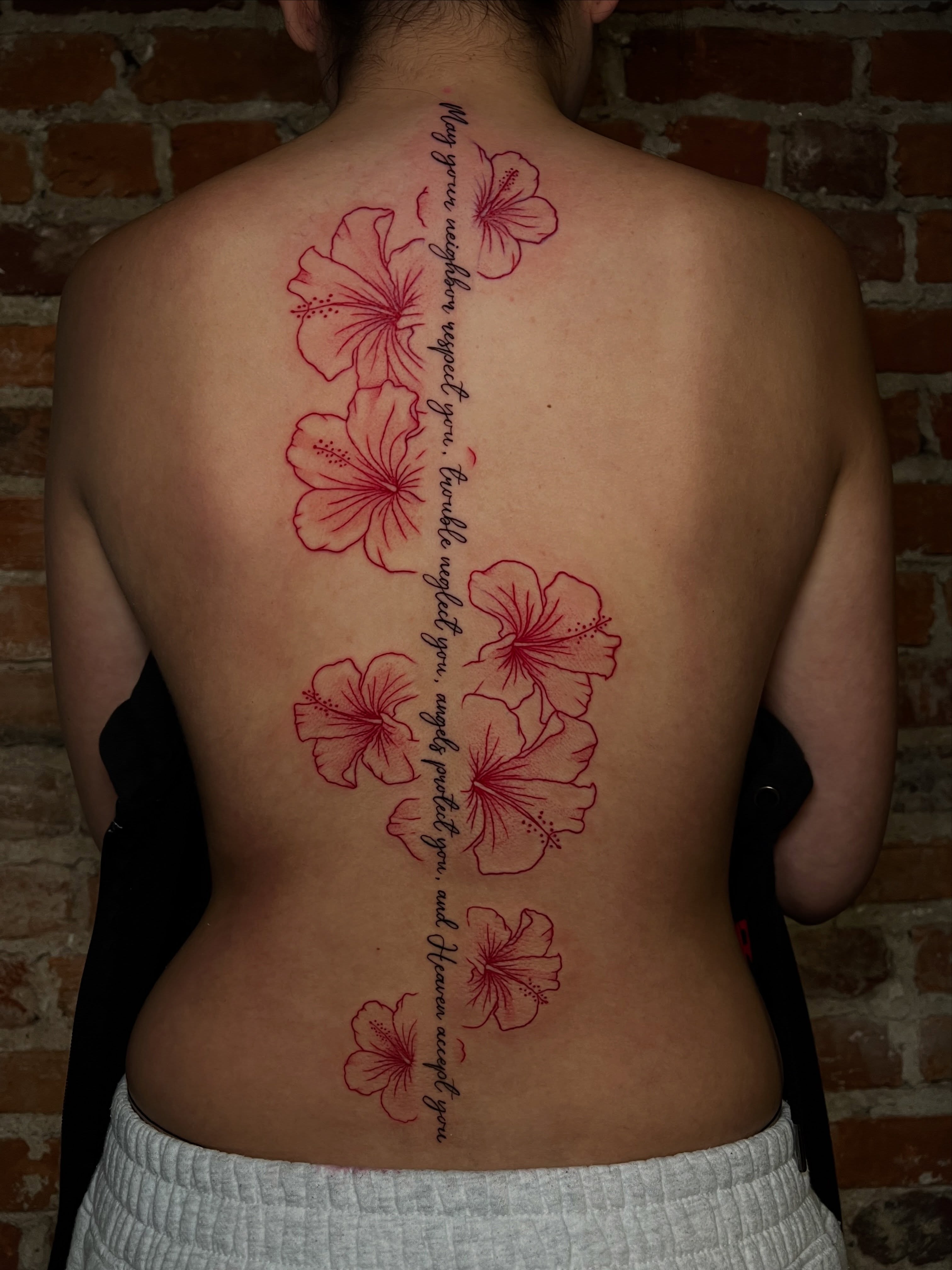 Hibiscus flowers and script fine line tattoo on the back by Uncomfy Comfort Tattoos LLC