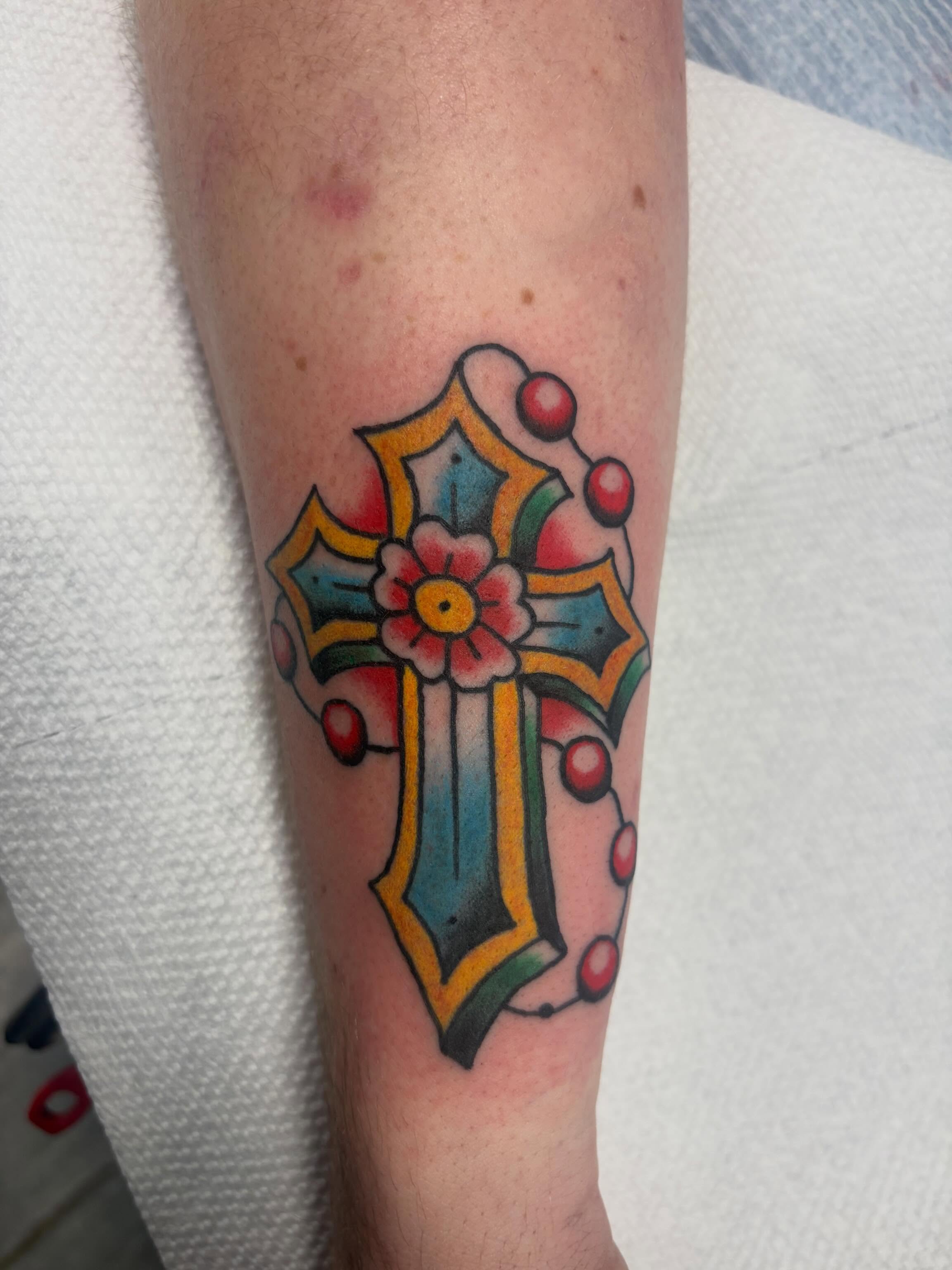 Cross with floral ornament American traditional tattoo on the forearm by Nolan Croteau