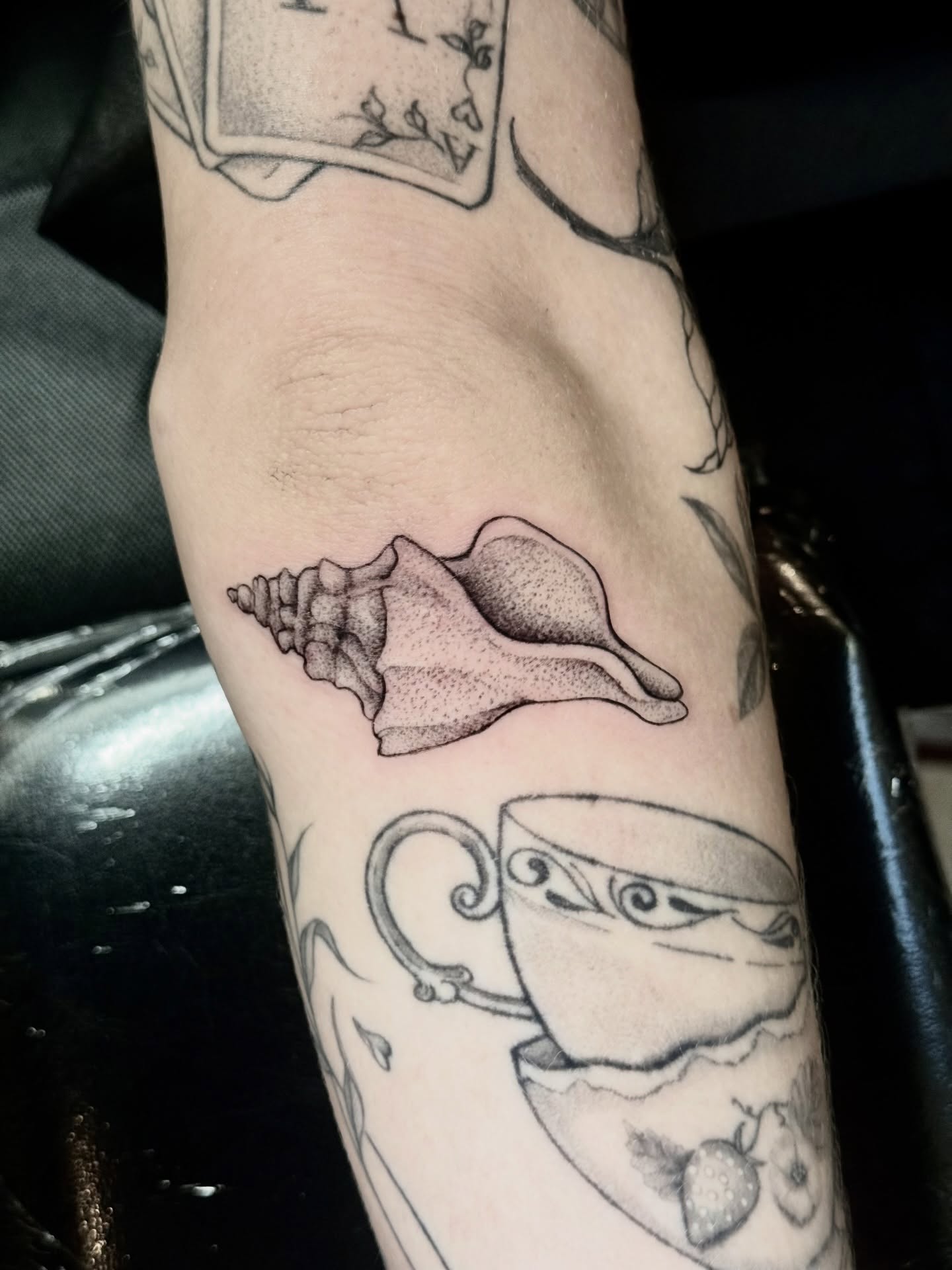 Shell and teacup black and grey tattoo on the forearm by ℳ𝒾𝓇𝓉𝒽𝒶 𝒯ℴ𝓇𝓇ℯ𝓈, San Diego, California