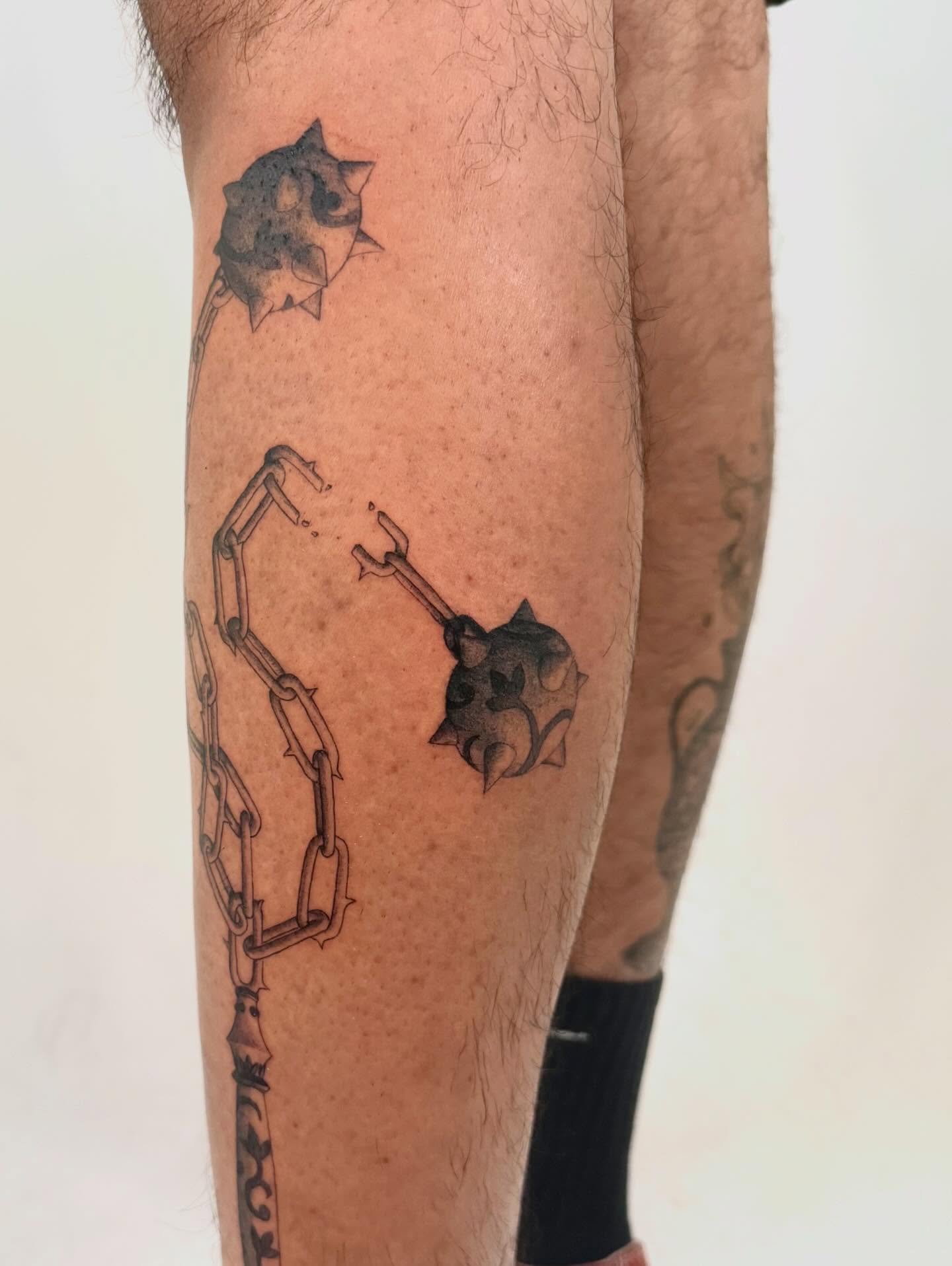 Chains and spiked ball black and grey tattoo on the calf by Andrew Flatts