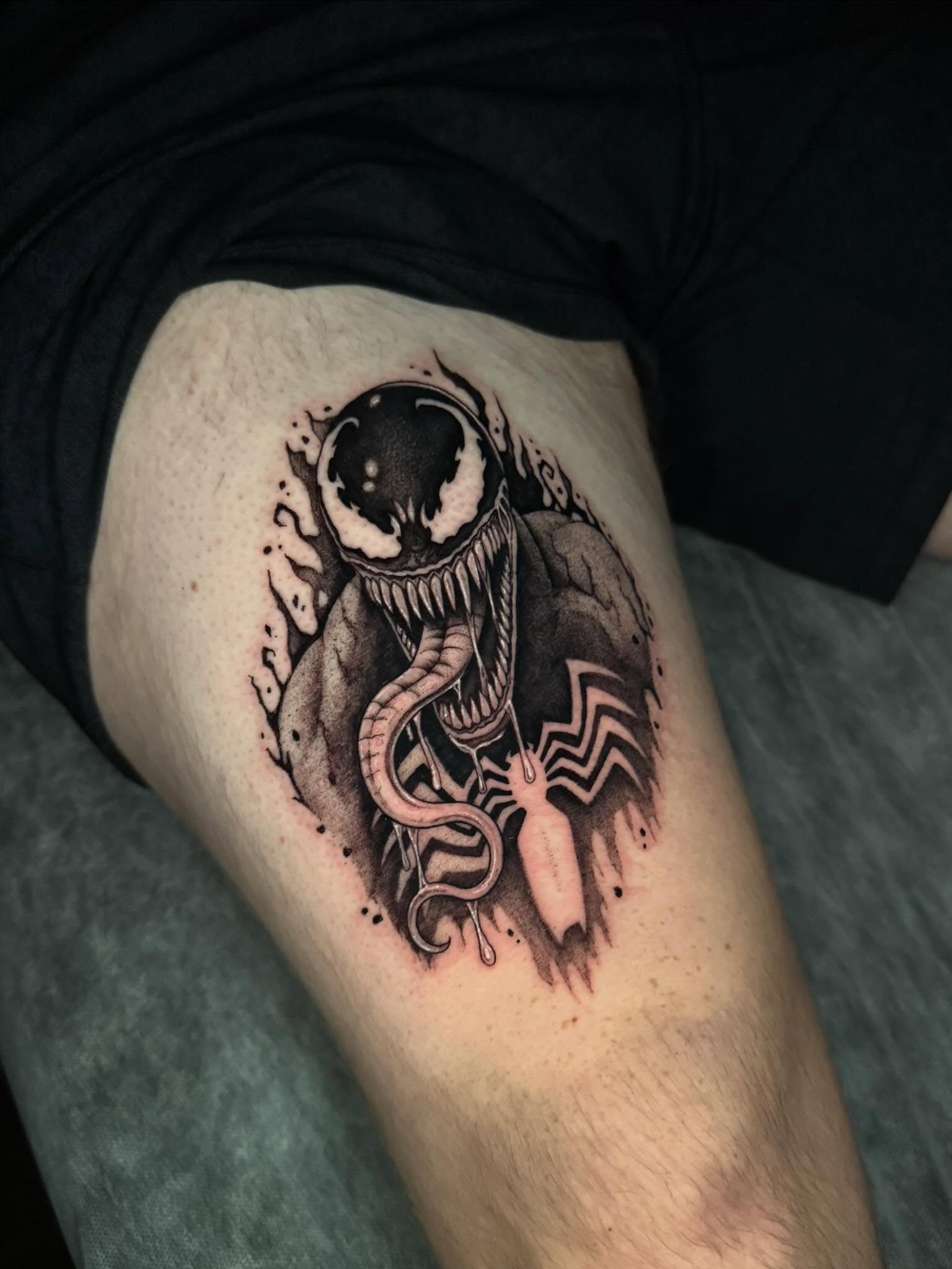 Venom black and grey tattoo on the thigh by kelsey hackett