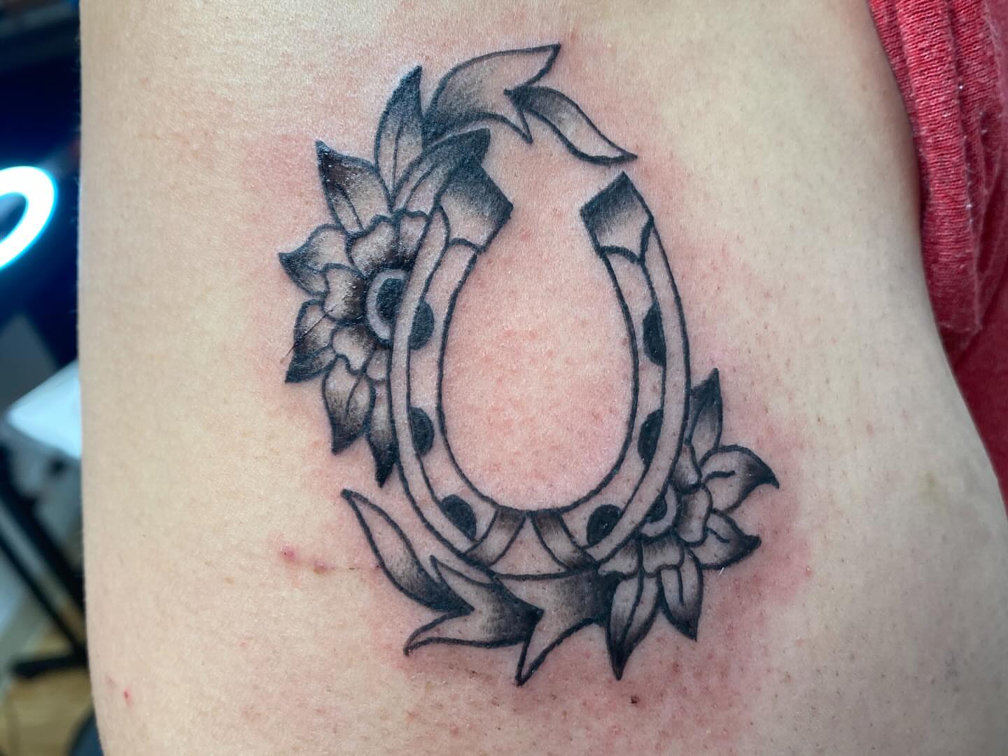 Horseshoe and floral wreath black and grey tattoo on the thigh by Laura🦋