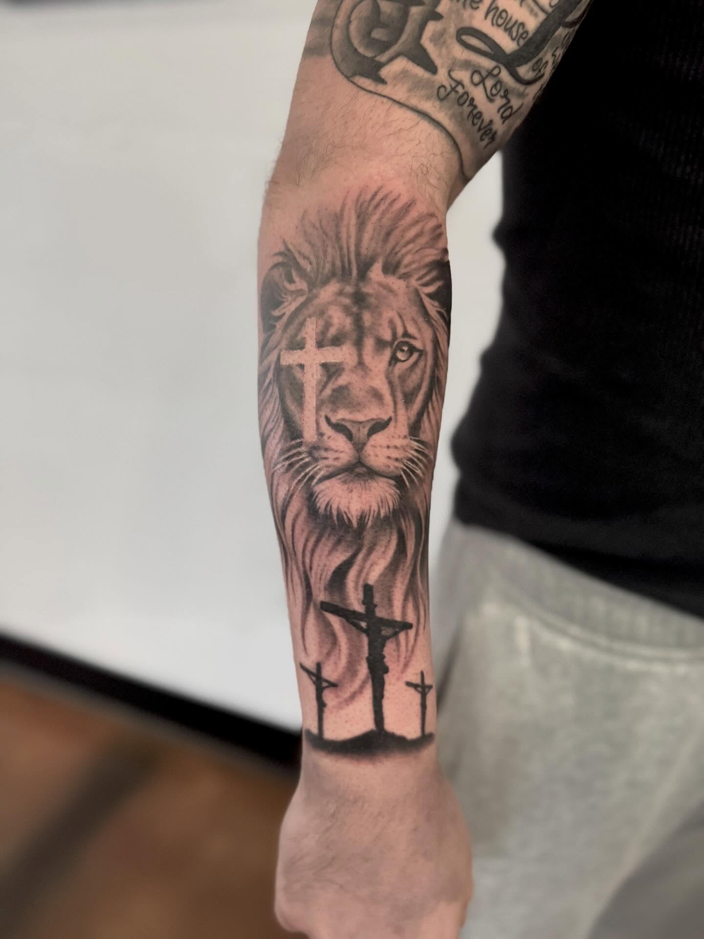 Lion and crucifixion realism tattoo on the forearm by Drew Foster, Toledo, Ohio