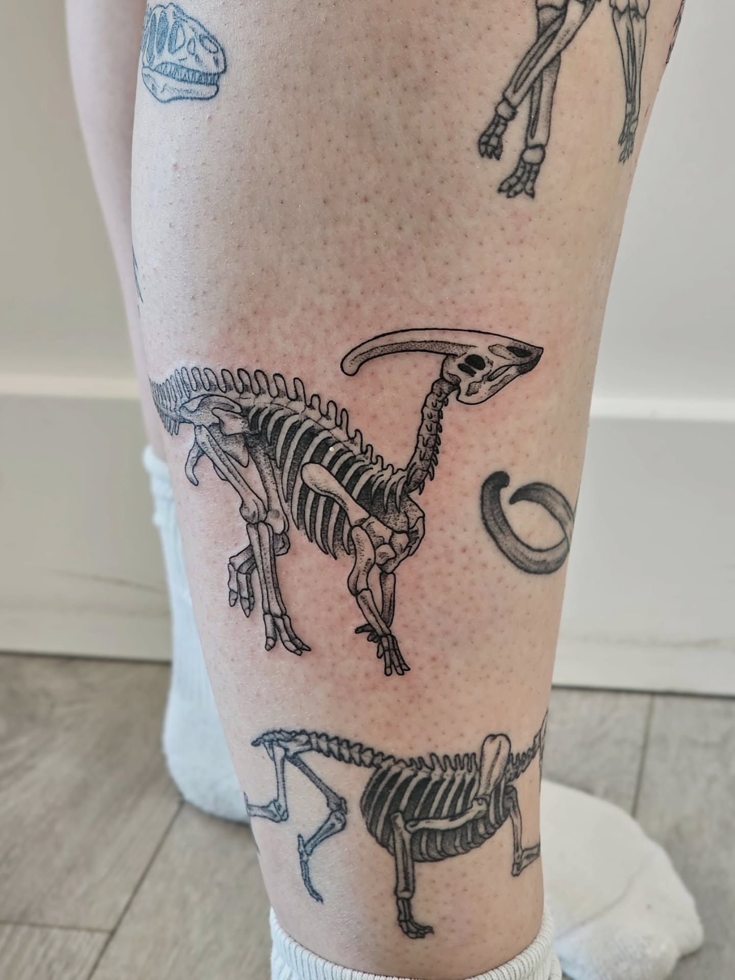 Dinosaur skeleton black and grey tattoo on the leg by Kylie Lund