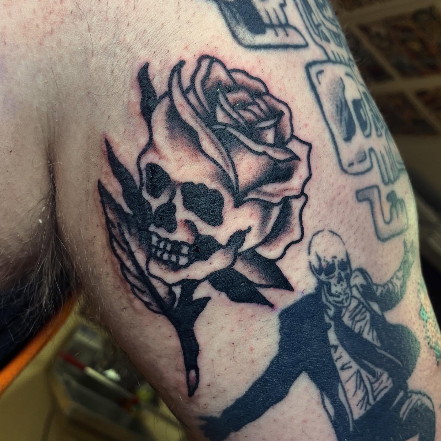 Rose with skull black and grey tattoo on the upper arm by Robert Morrow