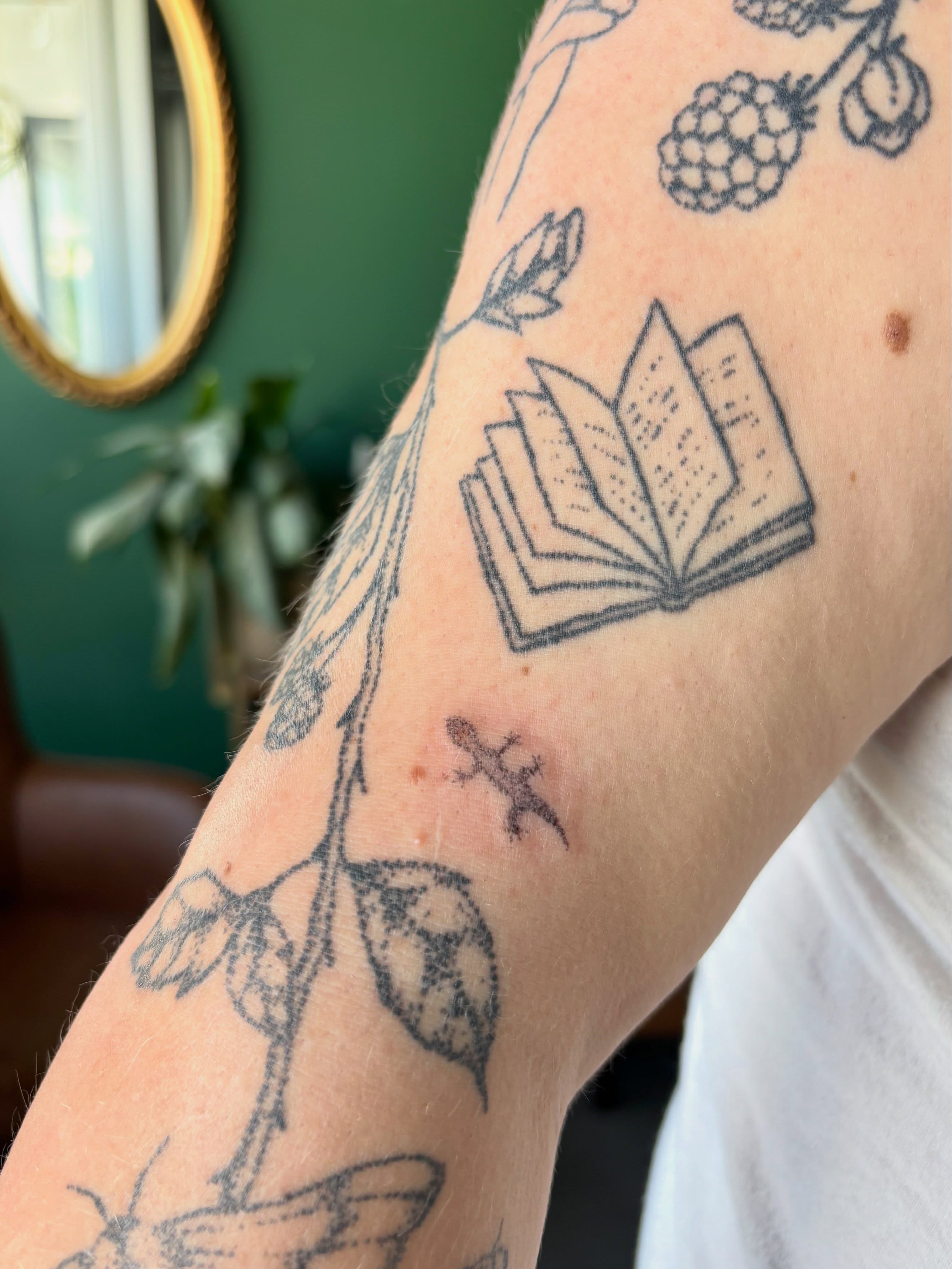 Book and botanical black and grey tattoo on the forearm by Ashley, Elk Horn, Iowa