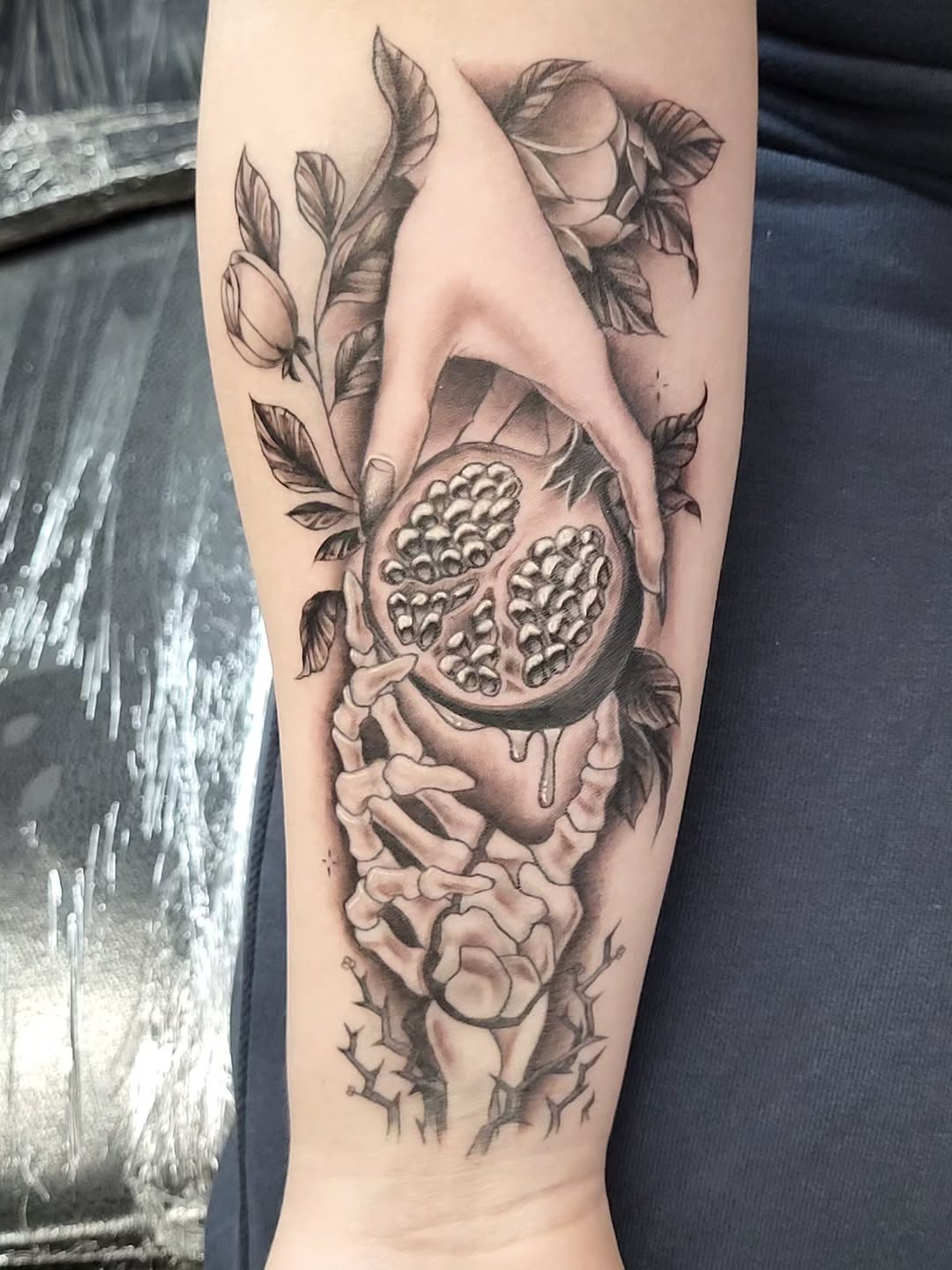 Hand holding pomegranate with skeleton hands dotwork tattoo on the forearm by TEA ☕️ Tattoos