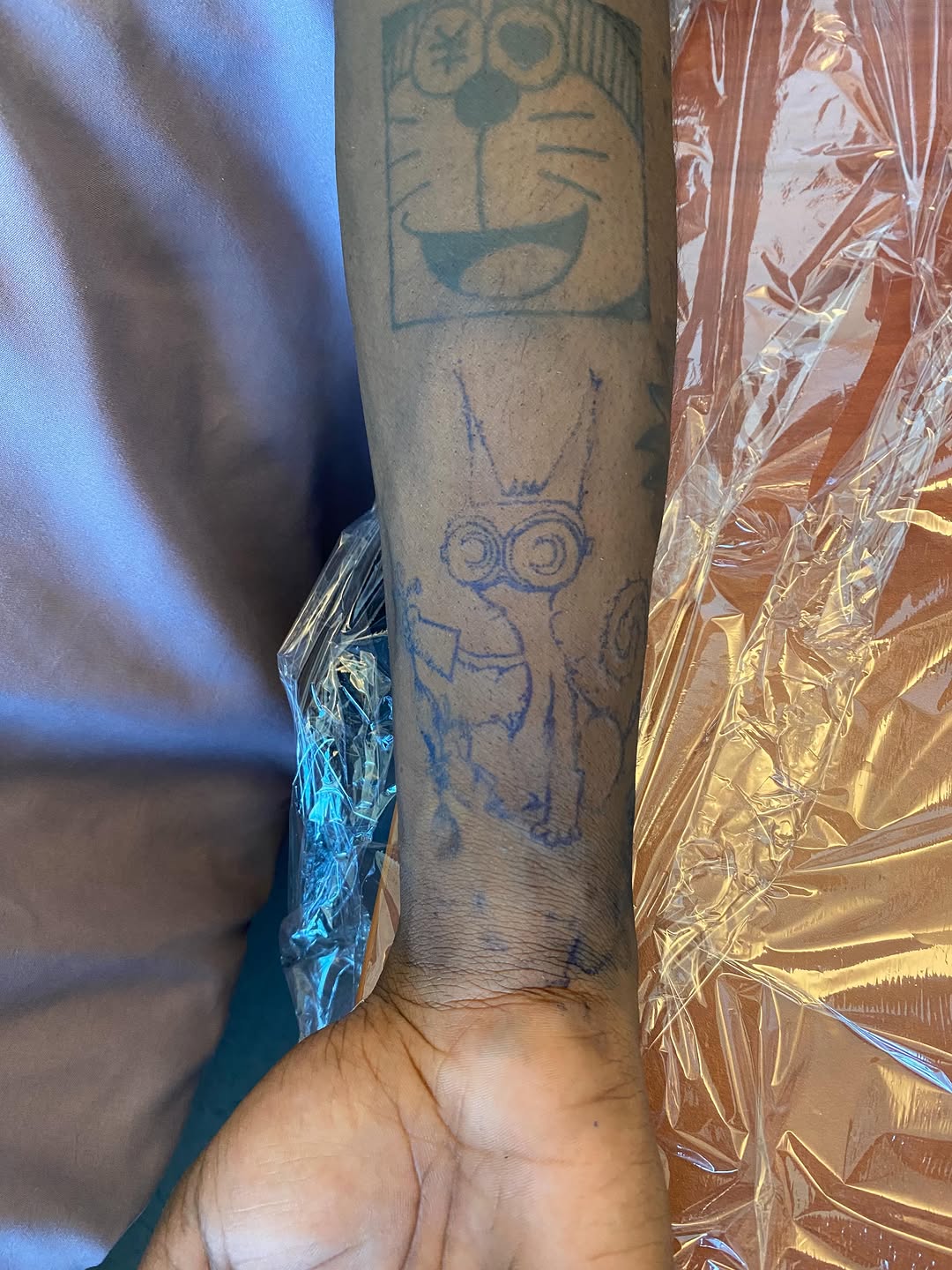 Doraemon and a cartoon character tattoo on the forearm by @feverfeverish