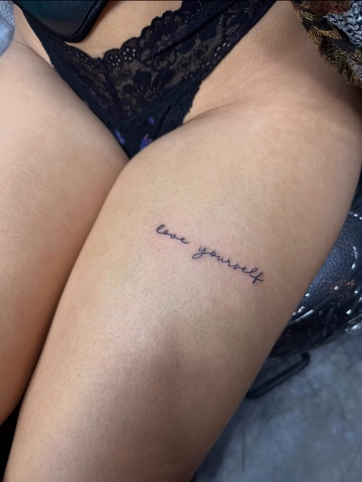 Thigh tattoo with text 'love yourself' lettering tattoo on the leg by Tony Hernandez, Chicago, Illinois