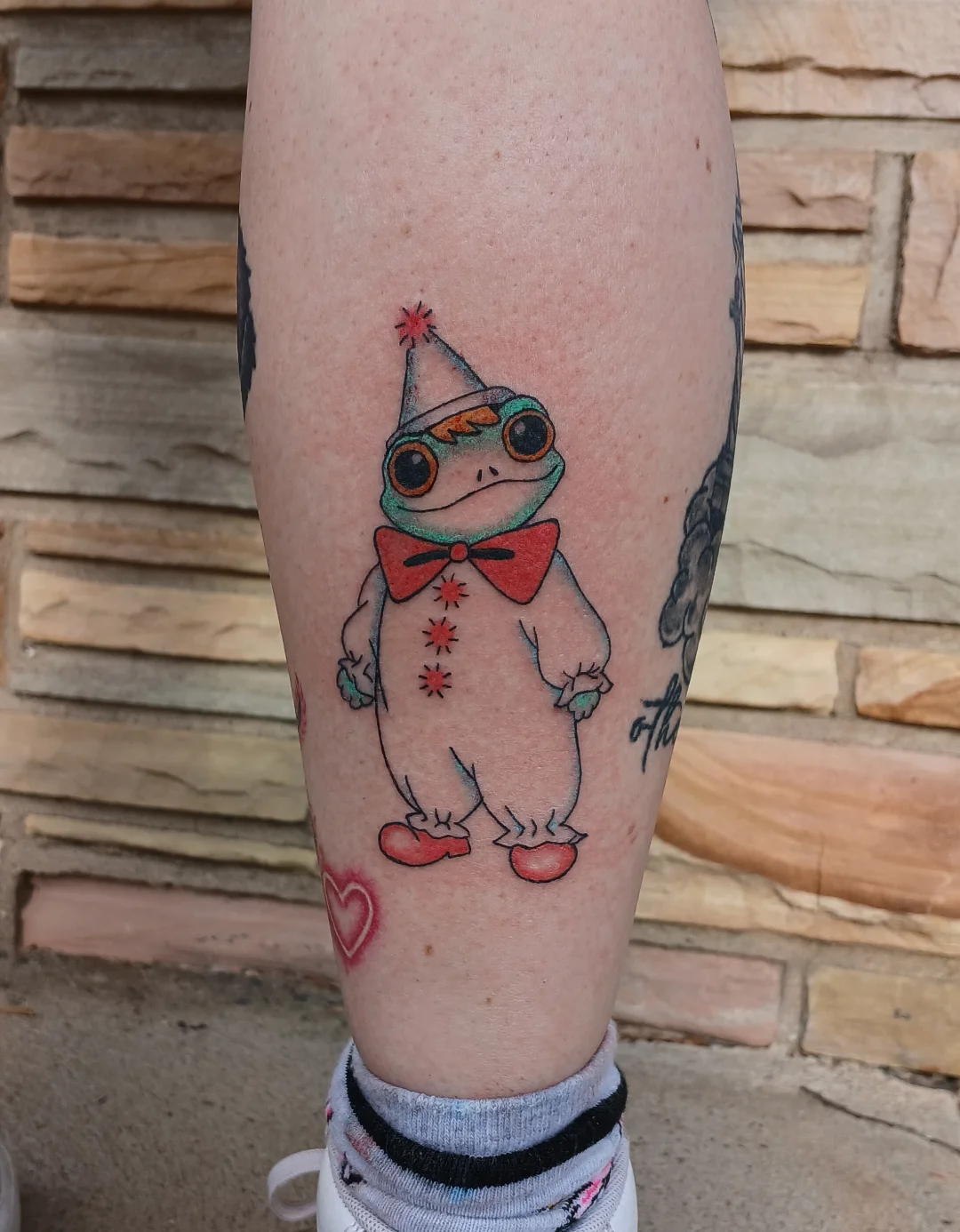Frog in clown costume trash polka tattoo on the calf by Amber Tattoos