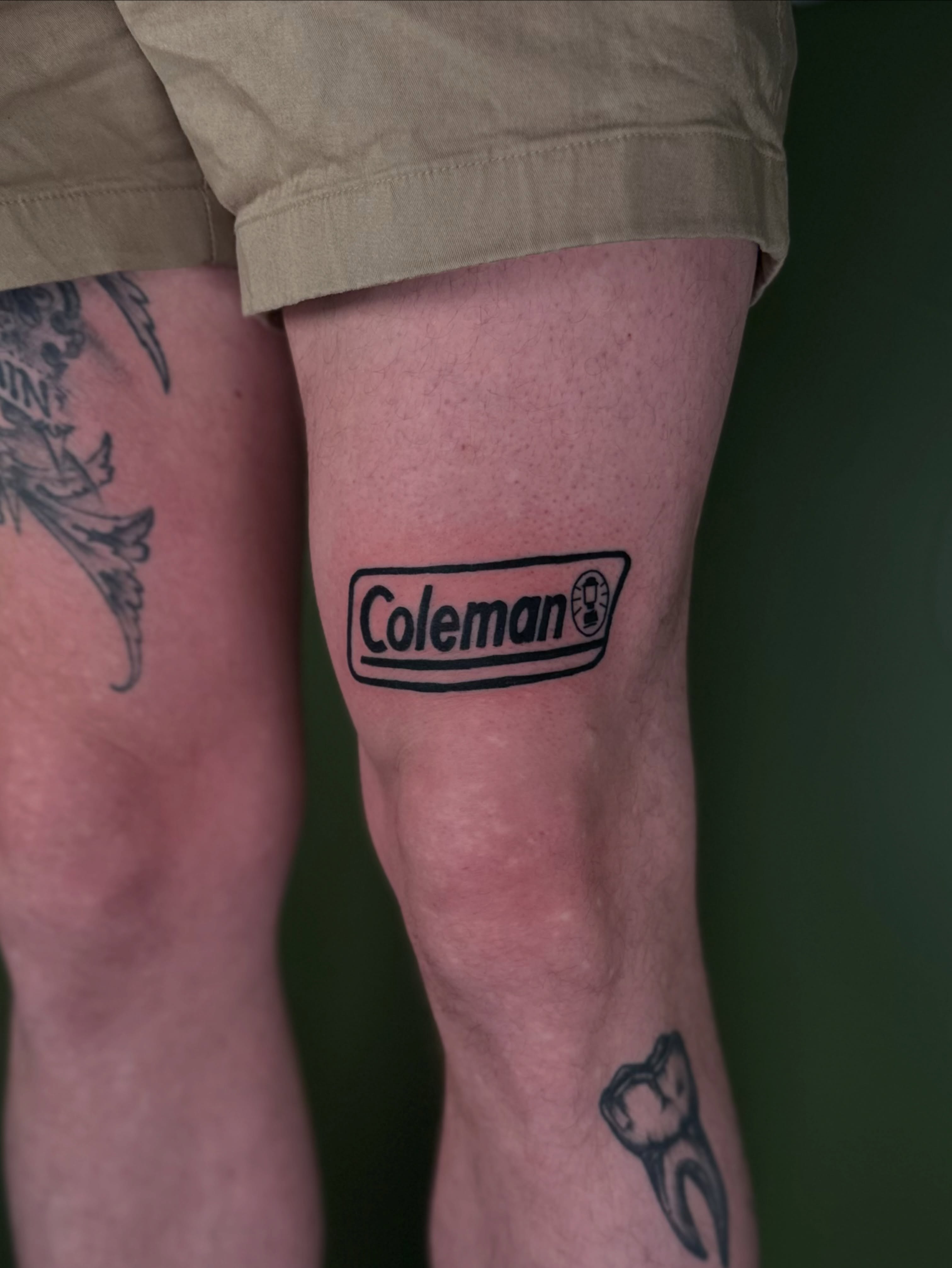 Coleman logo black and grey tattoo on the leg by Nikolas Tapio Aatos Mäkelä