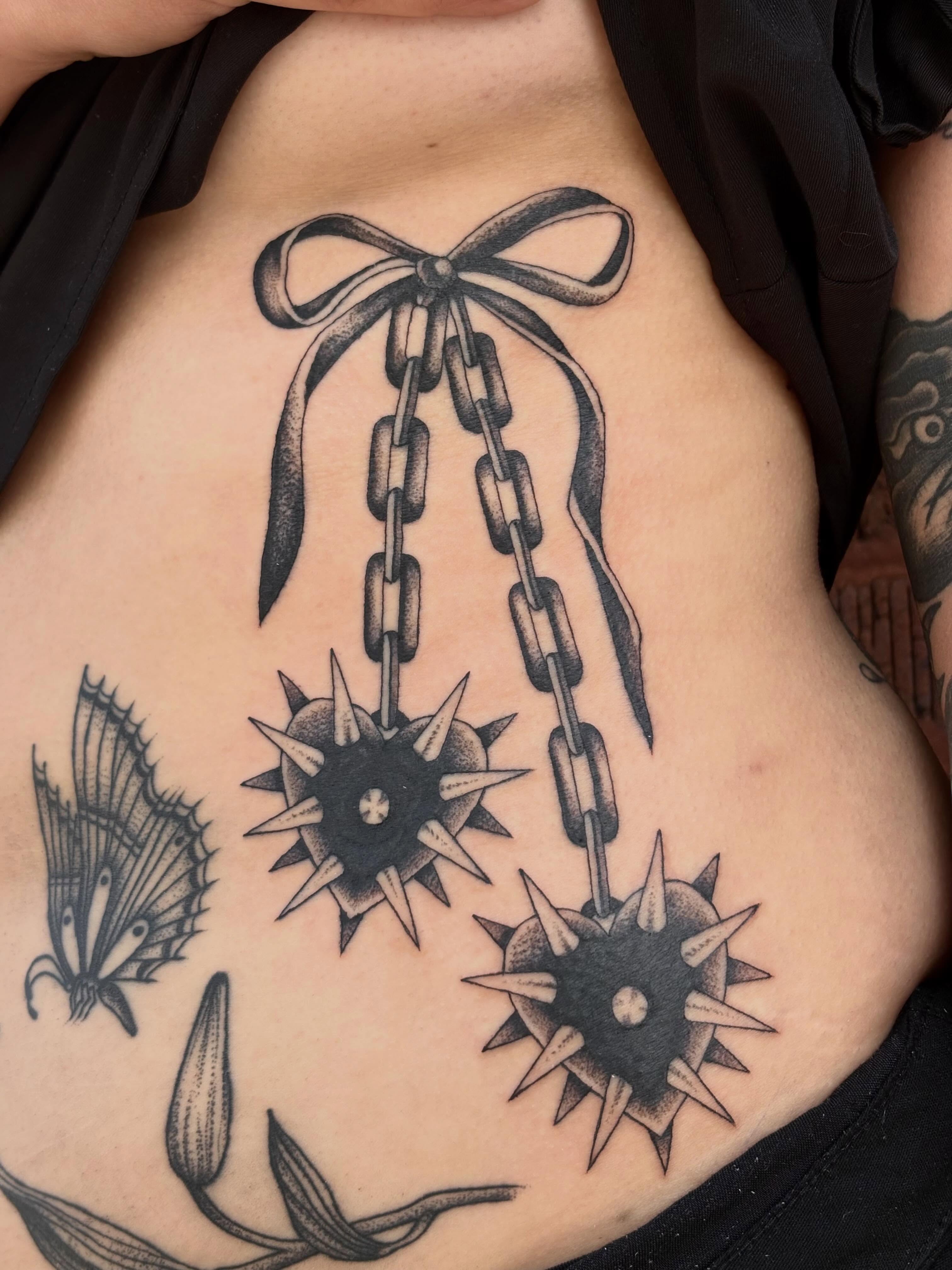 Chains and bow black and grey tattoo on the ribs by Sydney Pflaumer