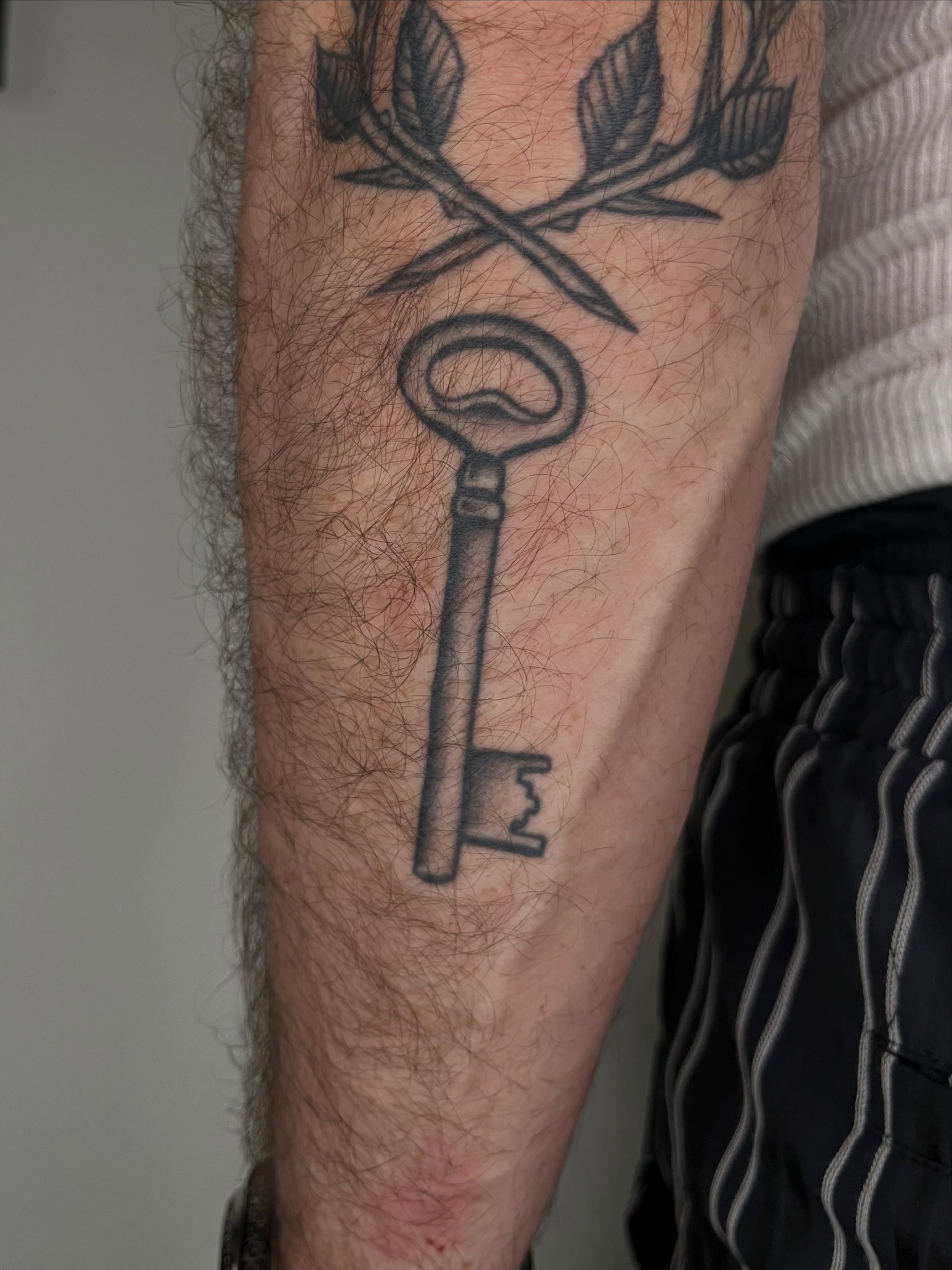 Key and crossed arrows black and grey tattoo on the forearm by Patrick Elijah