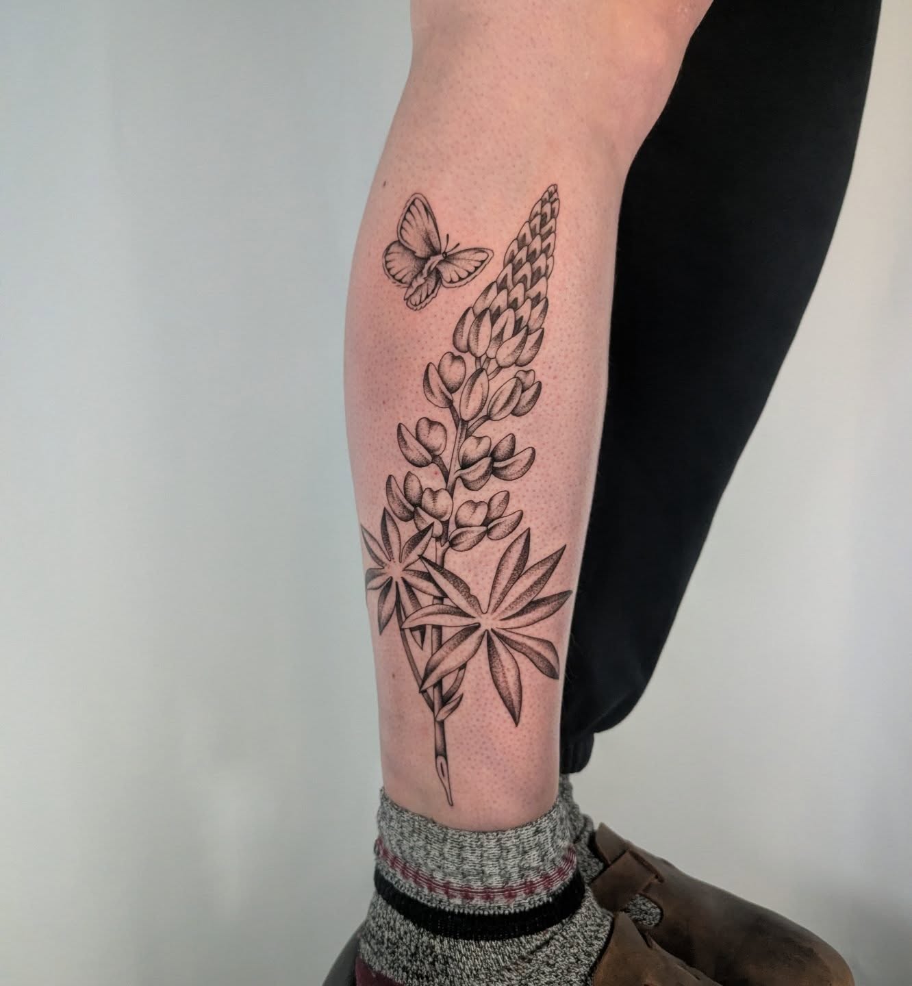 Lupine flowers and butterfly dotwork tattoo on the calf by Courtney Yaddof