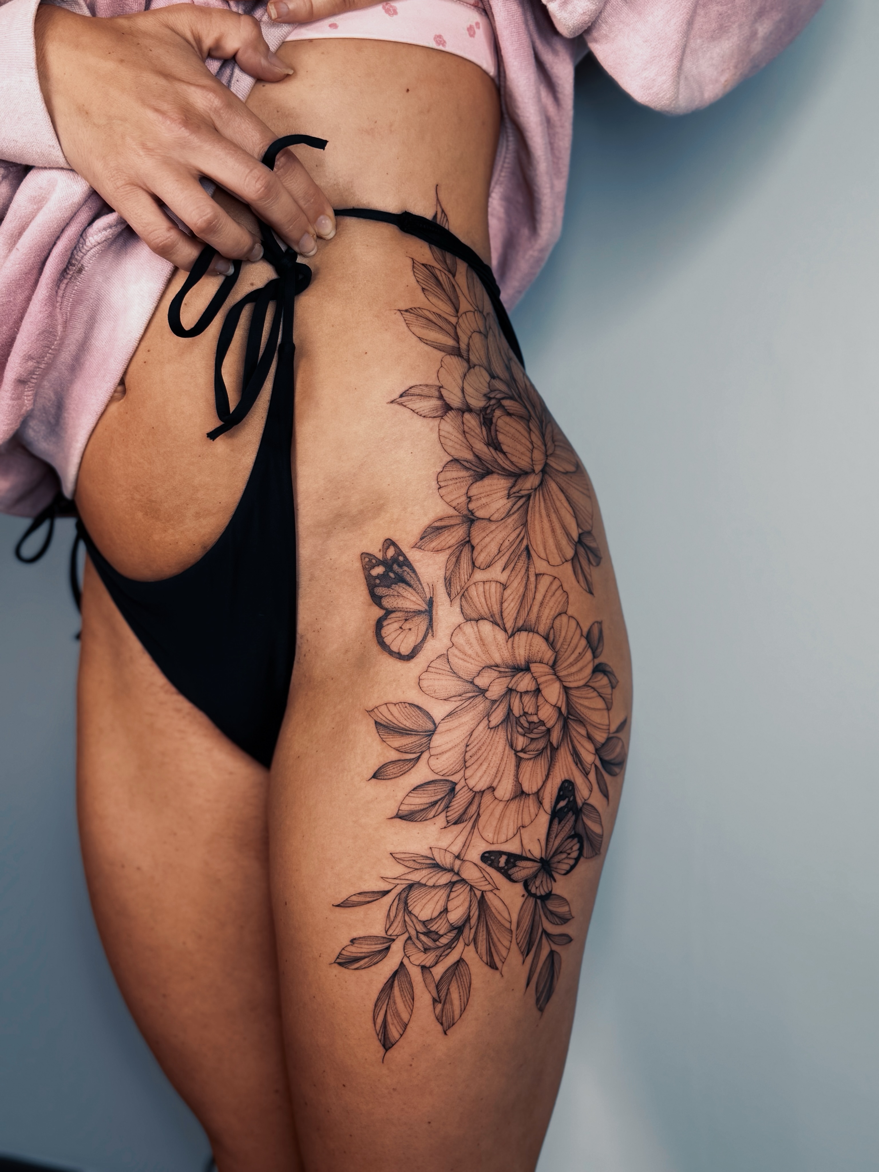 Floral bouquet with butterflies black and grey tattoo on the thigh by Olha Tytarenko