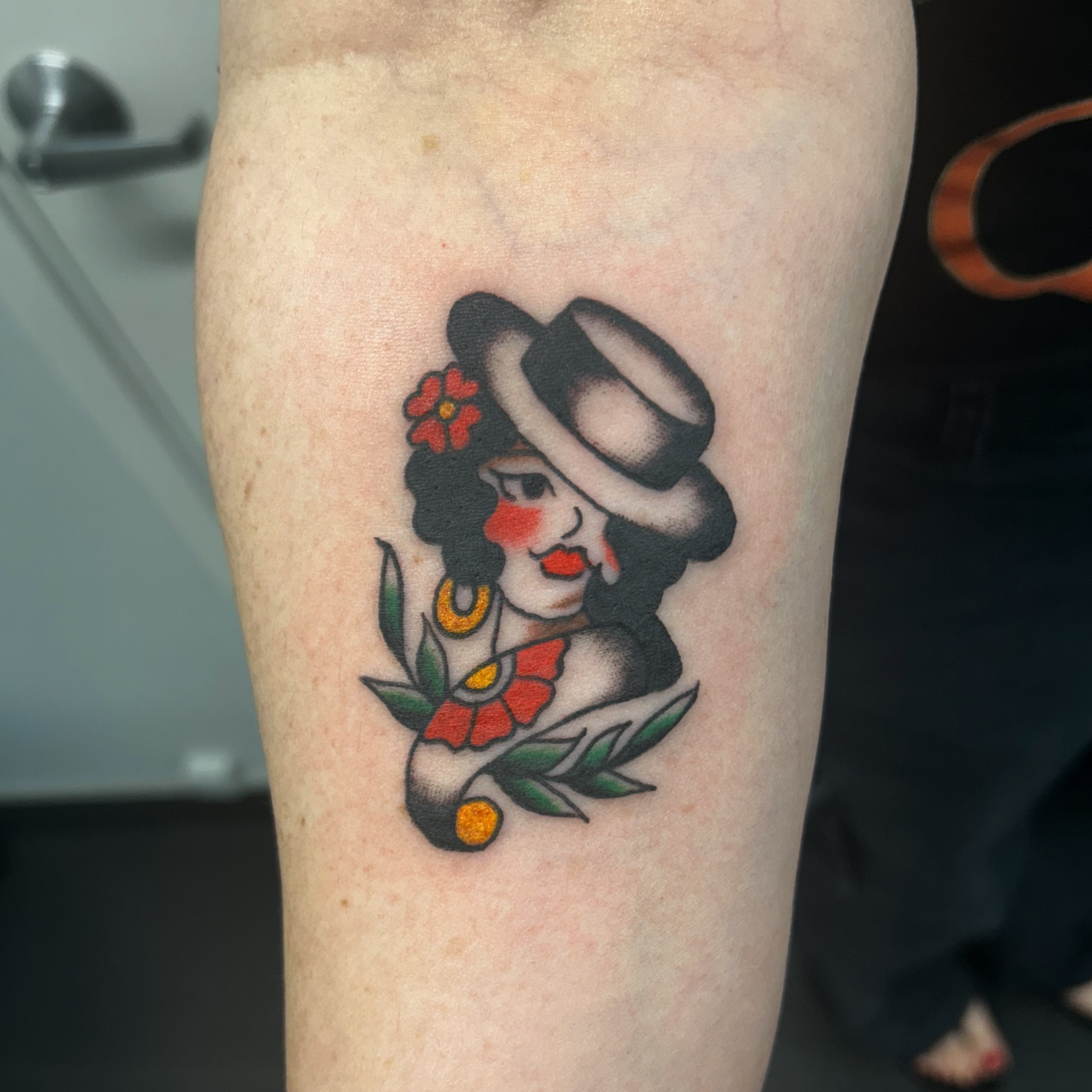 Woman wearing hat American traditional tattoo on the forearm by Tawni Bender