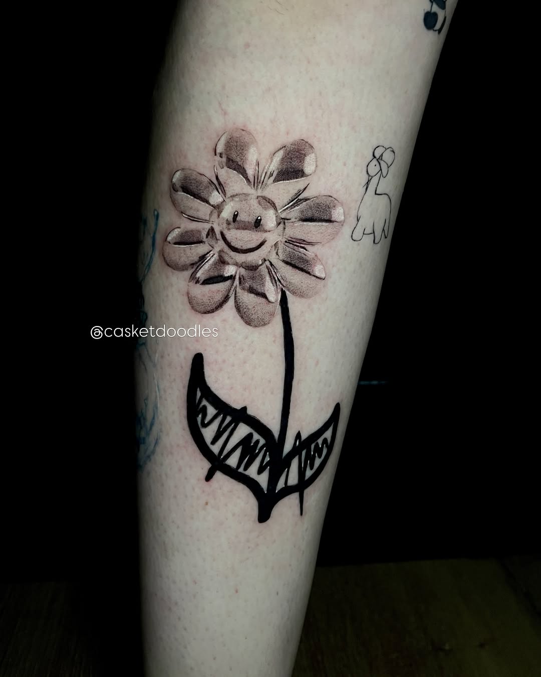 Flower with smiley face and doodle ignorant tattoo on the forearm by clarissa