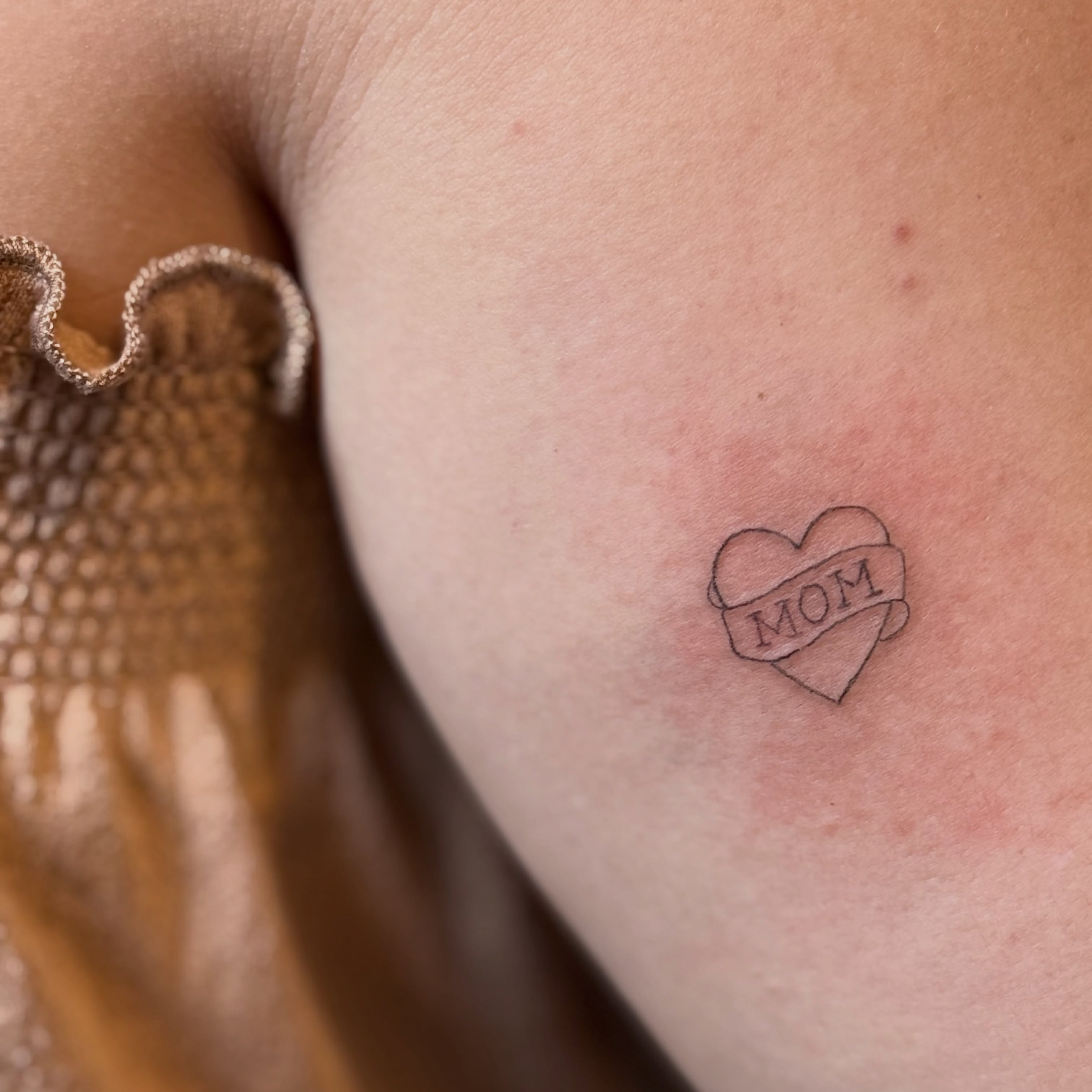 Heart with ribbon black and grey tattoo on the chest by Fineline Tattoo