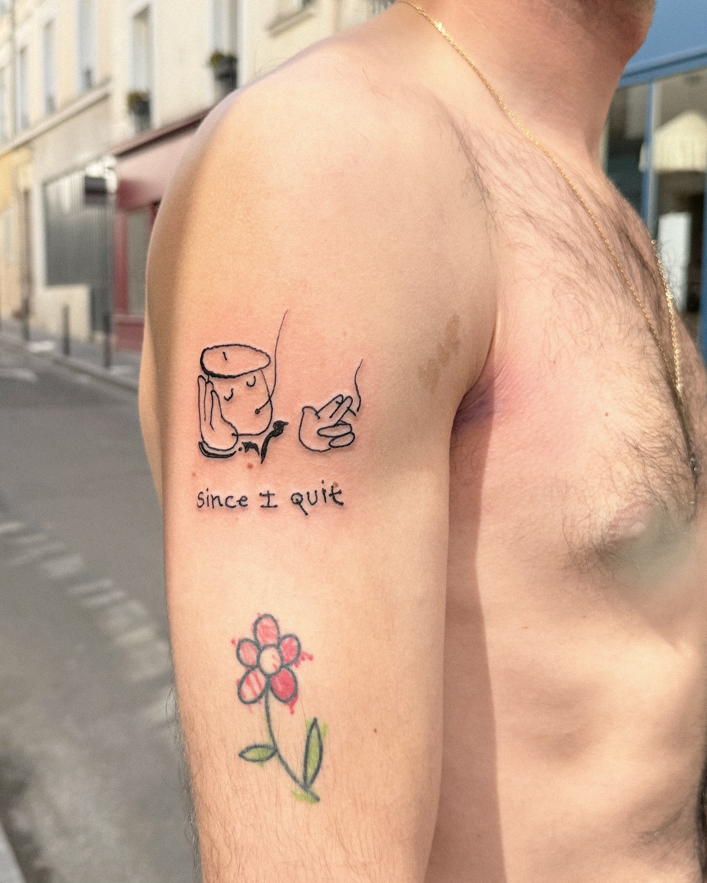 Coffee cup and flower fine line tattoo on the upper arm by Eden Kalif