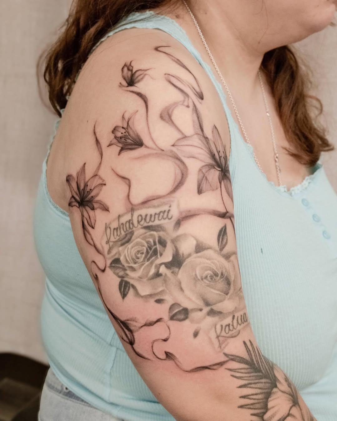 Flowers and script black and grey tattoo on the upper arm by Koko