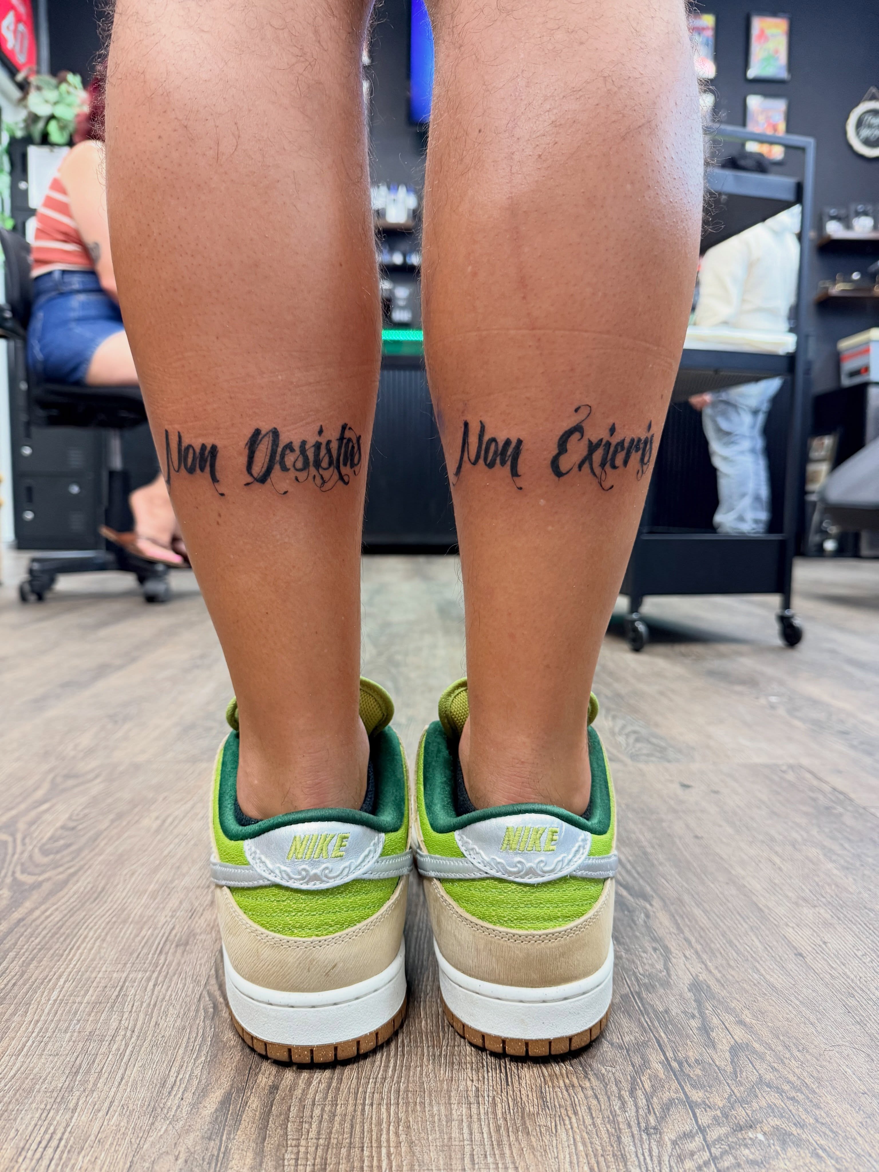 Non desistas non exieris lettering script tattoo on the leg by Chris
