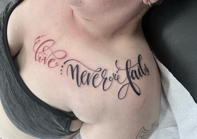 Love never fails lettering script tattoo on the chest by El Kapitan