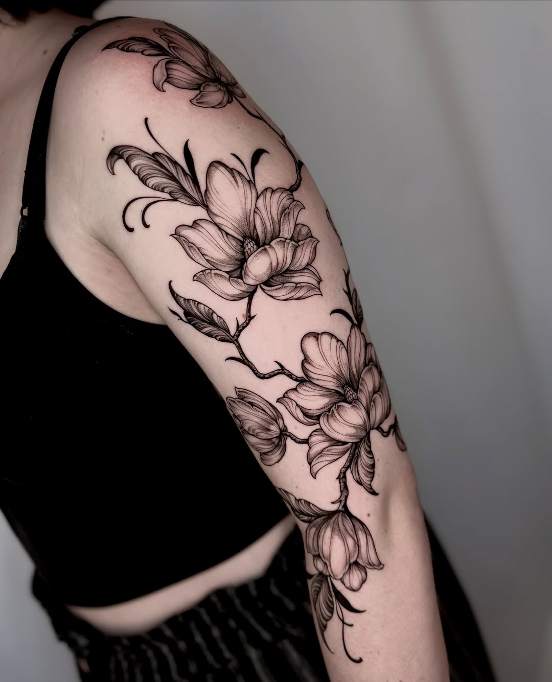 Magnolia flowers fine line tattoo on the upper arm by Kathryn Semus
