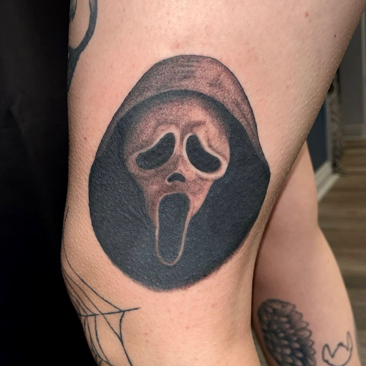 Scream mask black and grey tattoo on the thigh by Elena