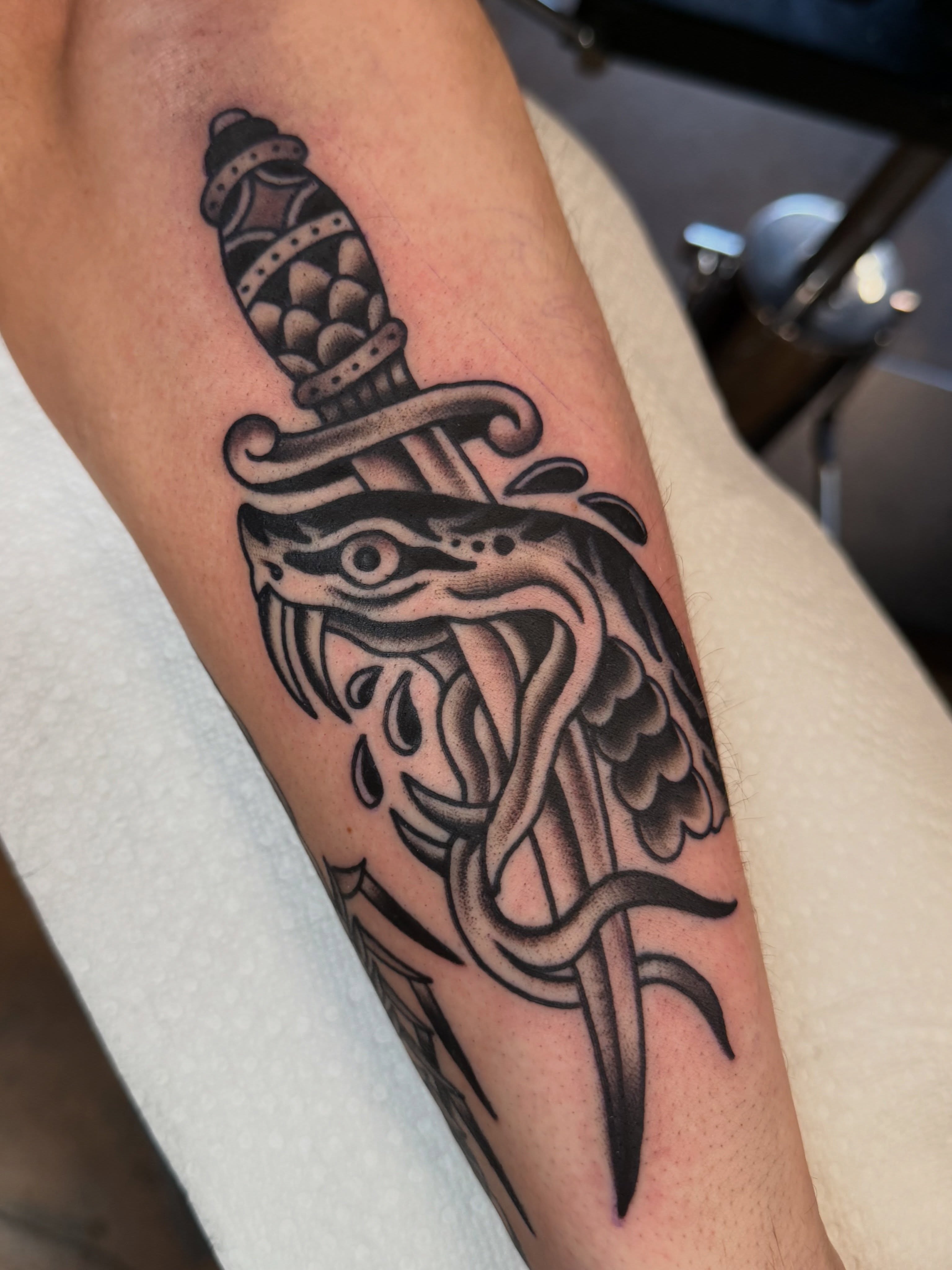 Snake and dagger black and grey tattoo on the forearm by Christopher Mikesell